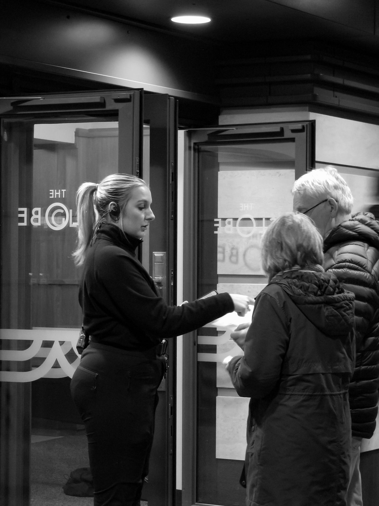 Action photo of a female security guard for Hinson Security Services scanning customer’s tickets at a theatre. Black and white.