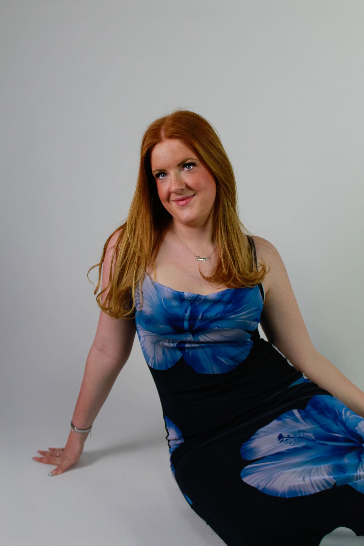 Studio portrait of a woman sat smiling. Fashion photo. Wearing a blue floral dress.