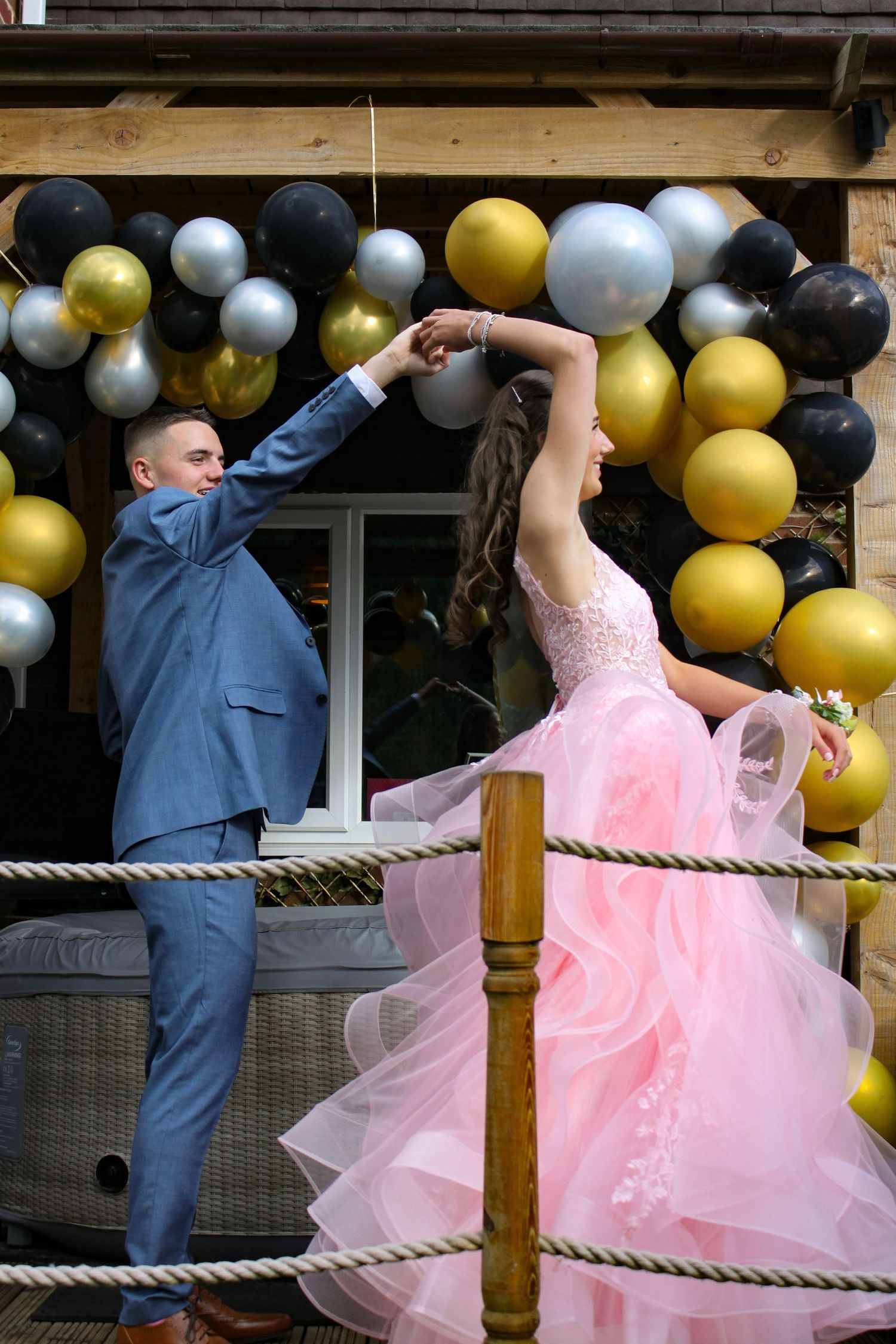 A couple on their prom day dancing. His suit is blue and her prom dress is pink.