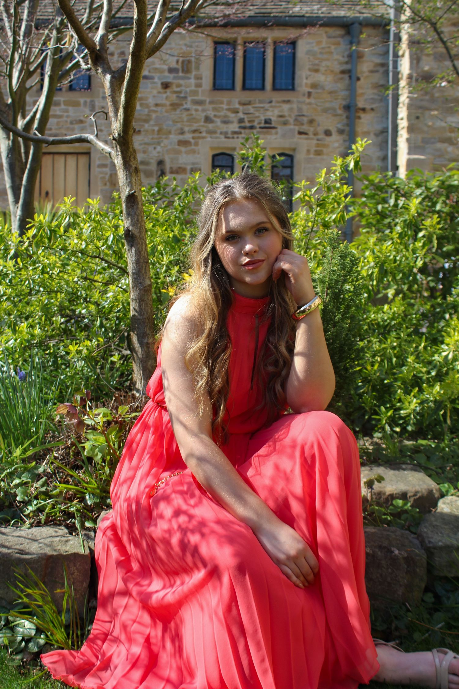 Editorial fashion portrait of a woman posed a garden with a beautiful background. Wearing her hair half up and a pink dress.