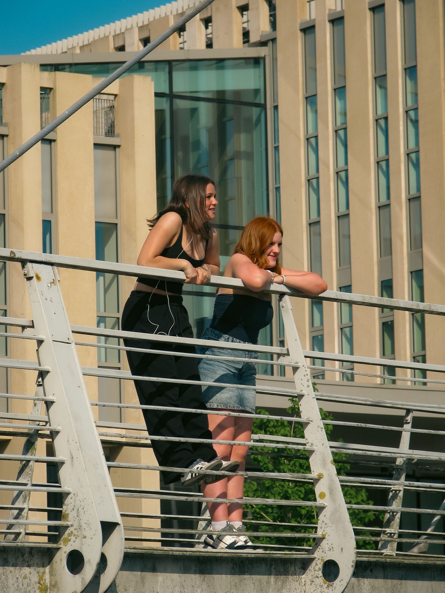 Street photography. Two women laughing on a bridge. Building behind them.