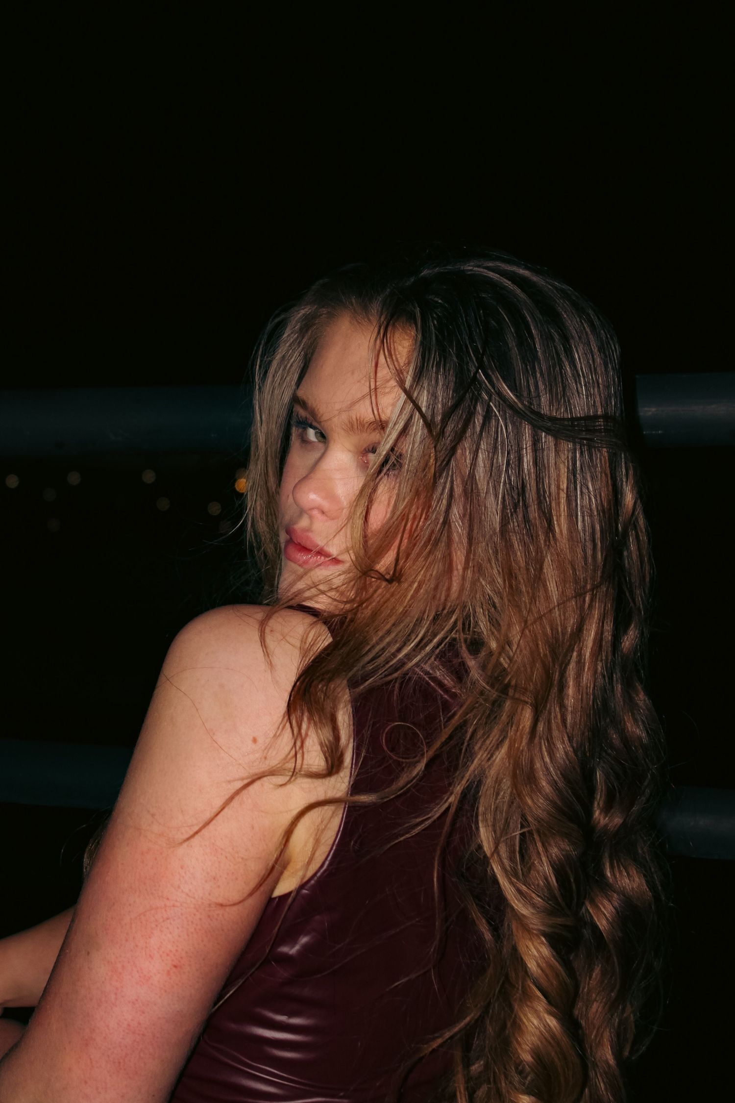 Editorial portrait photoshoot of girl wearing burgundy dress at night. Looking over the shoulder pose. Flash lighting.