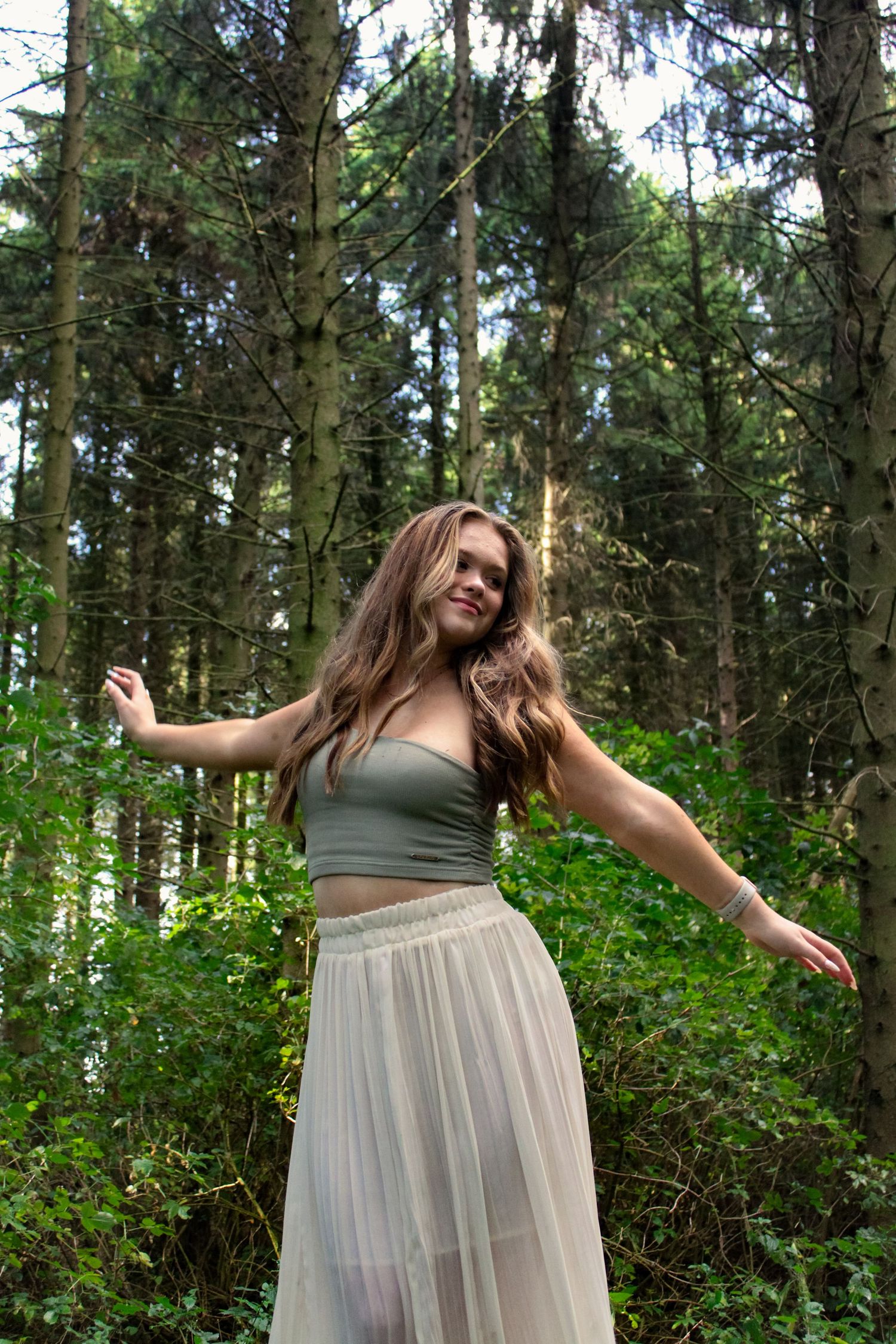 A photo of a woman dancing in a forest wearing a green top and white skirt.