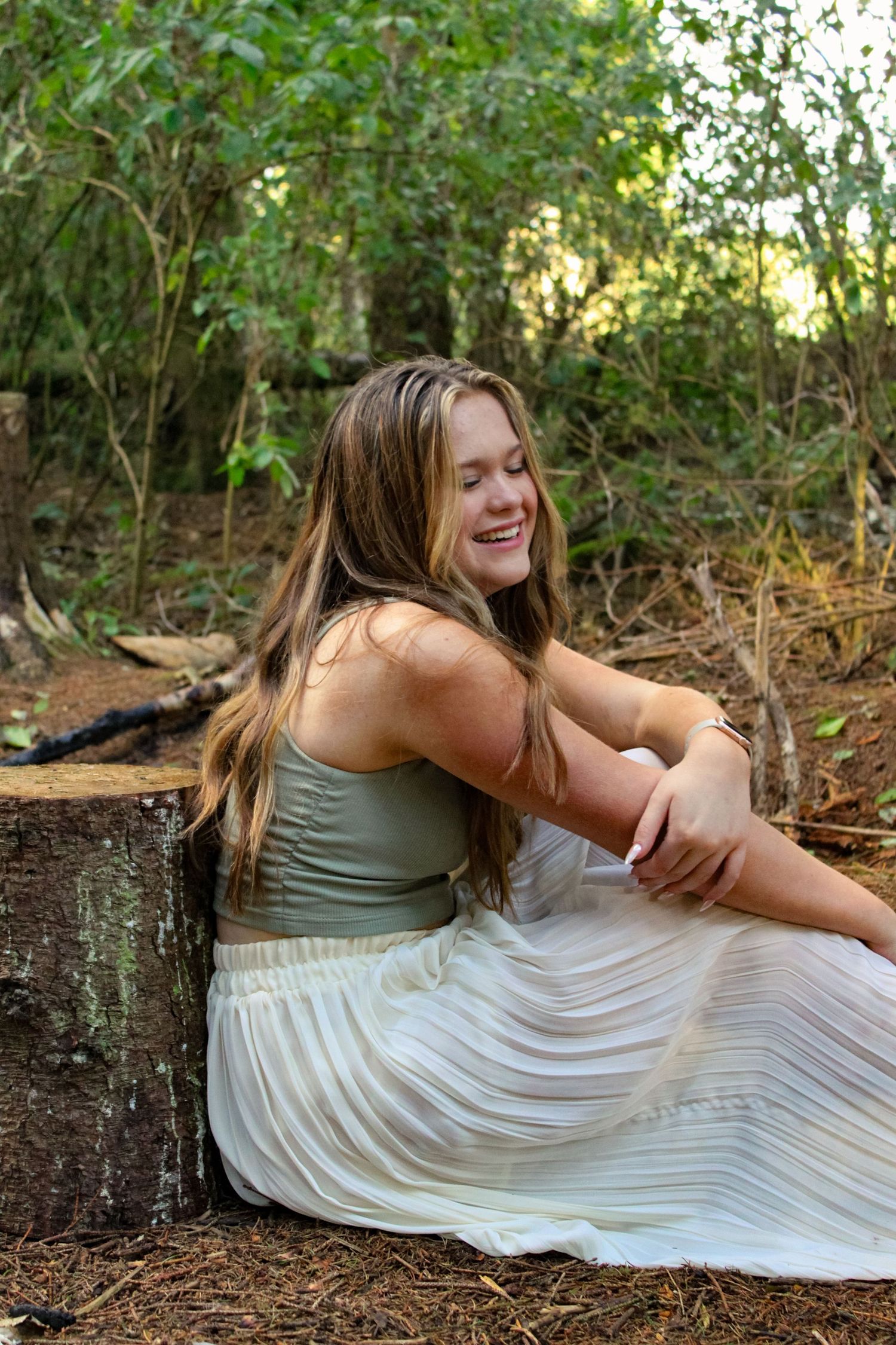 Portrait of woman sat in a forest and smiling. Golden hour lighting.
