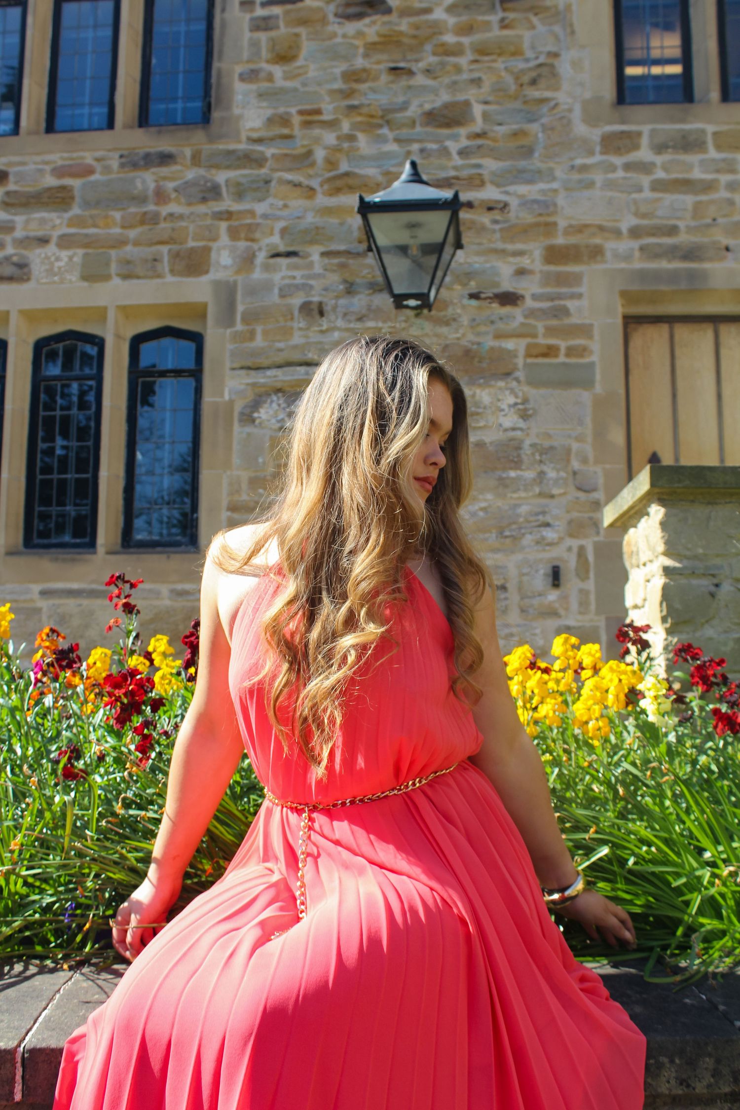 Editorial fashion portrait of a woman posed a garden with a beautiful background. Wearing her hair down and a pink dress.