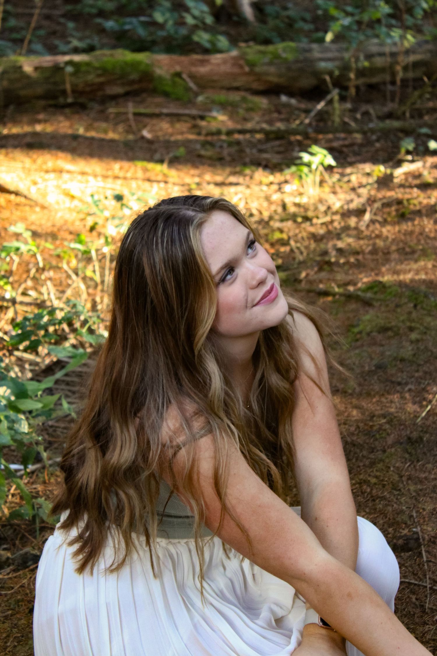 Portrait of woman crouched in a forest and smiling. Golden hour lighting.