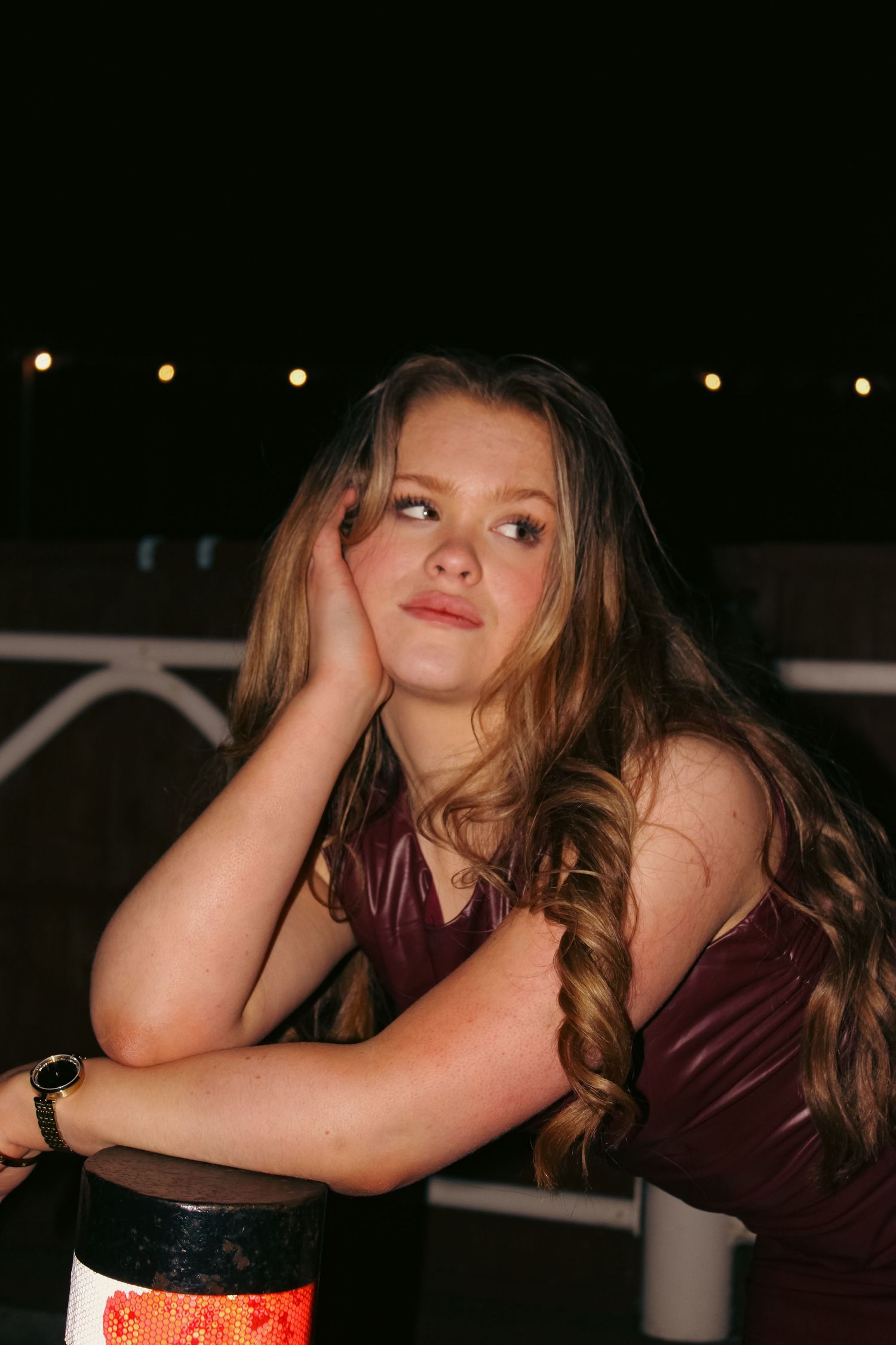 Editorial portrait photoshoot of girl wearing burgundy dress at night. Relaxed pose. Flash lighting.