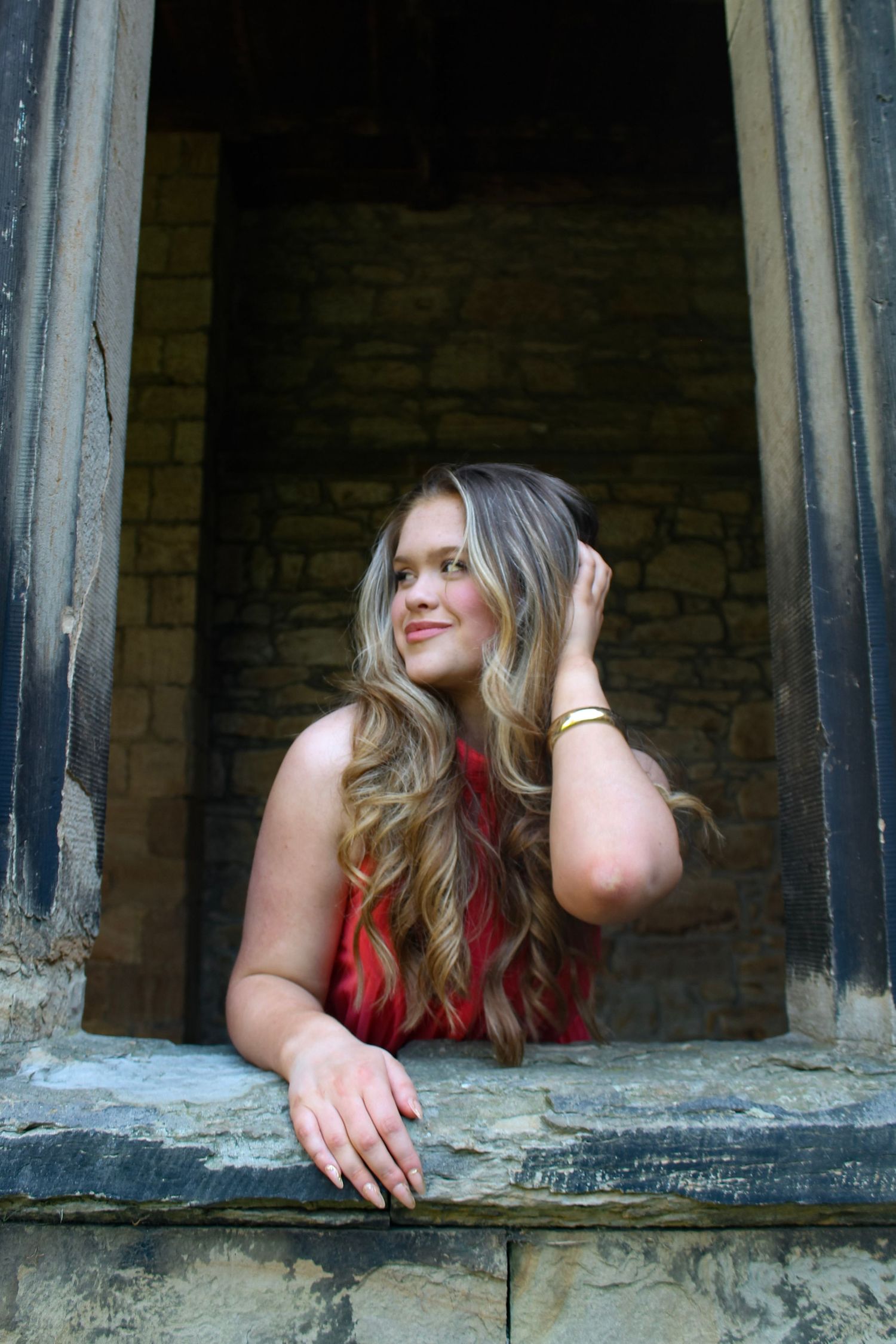Editorial fashion portrait of a woman looking out of a window in Durham Cathedral. Wearing her hair down and a pink dress.