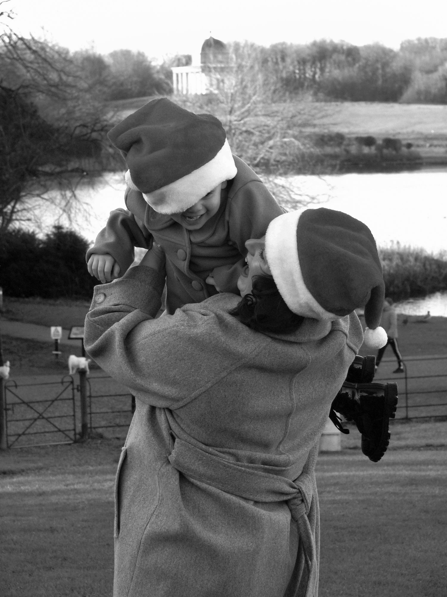 A mother hugging her daughter. Both are smiling and wearing Santa hats. Family photoshoot. Black and white.