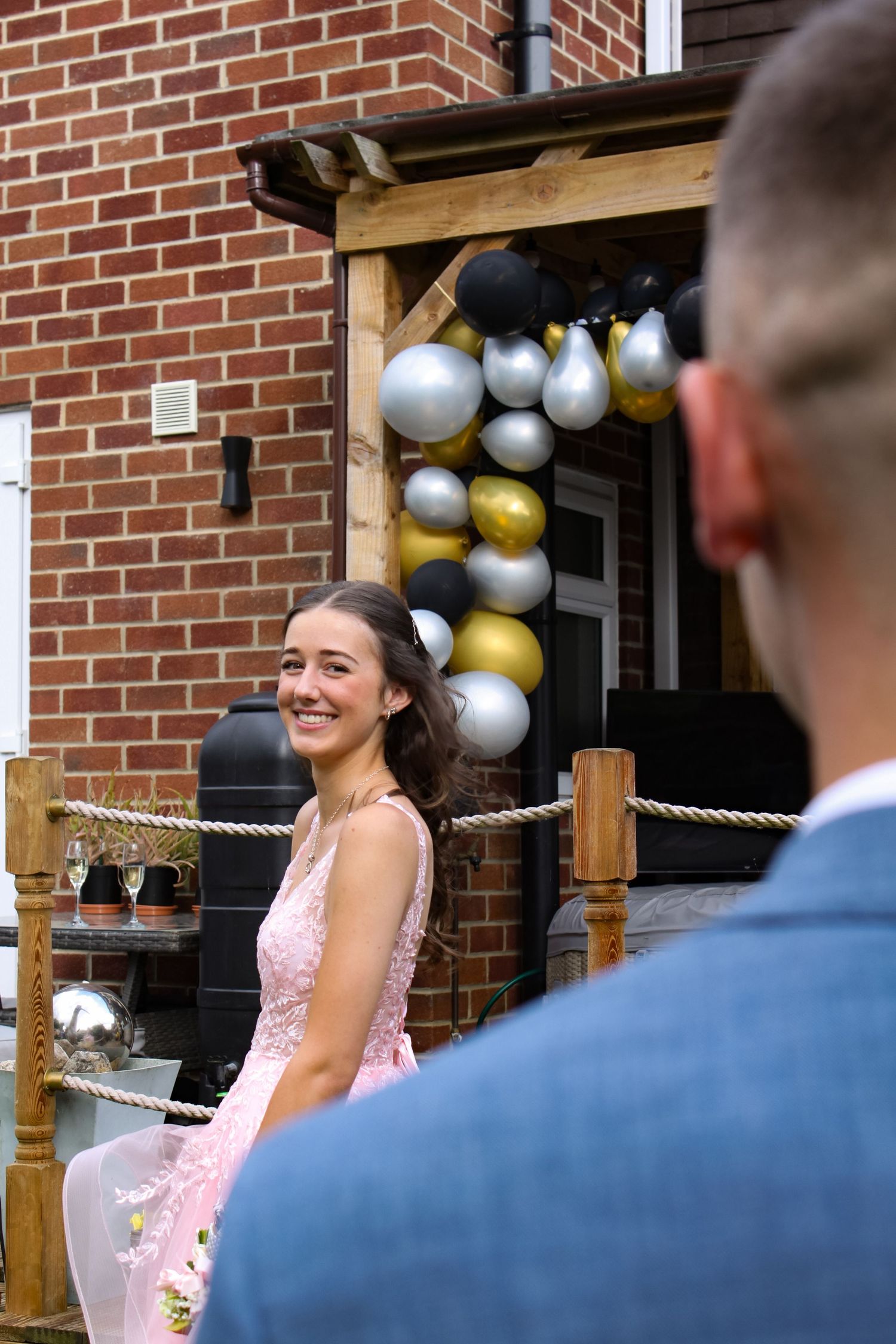 A prom photo of a couple. The girl is looking at her partner and smiling. His suit is blue and his tie is pink. Her dress is pink.