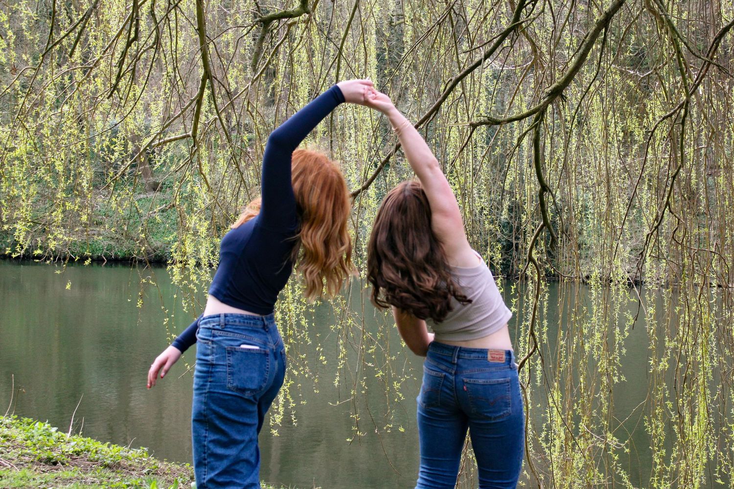 Candid photo of two girls dancing with a beautiful river behind them under a willow tree.