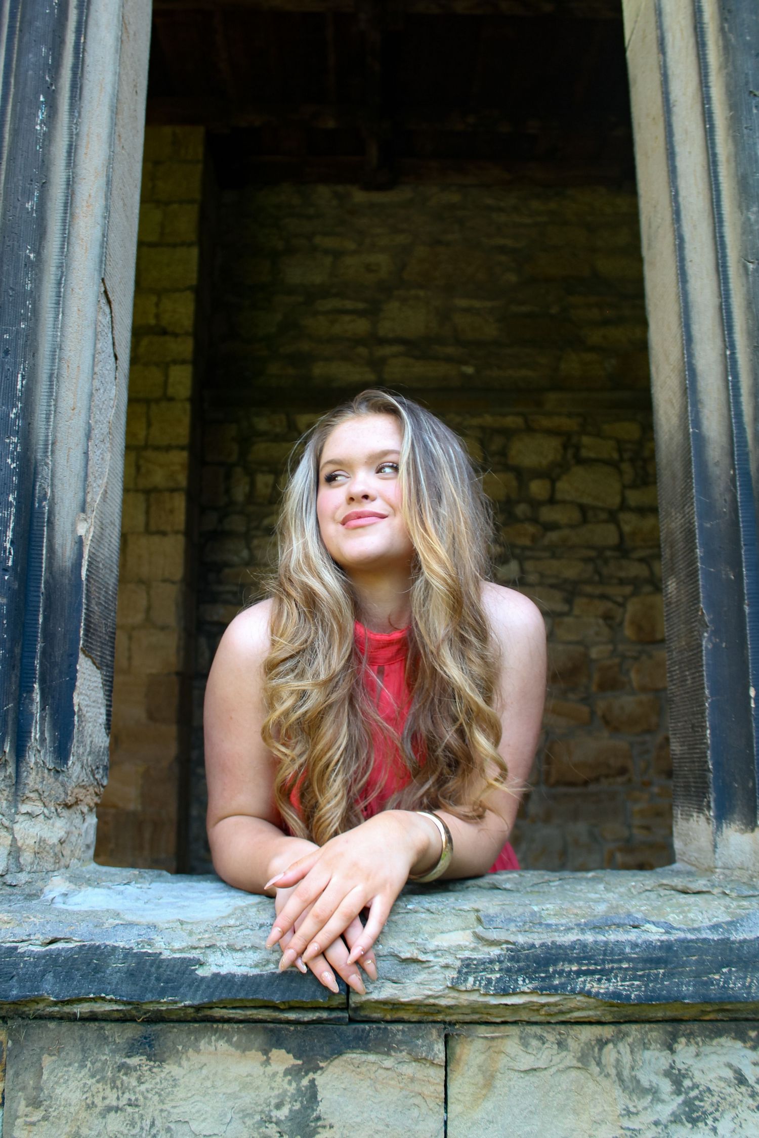 Editorial fashion portrait of a woman looking out of a window in Durham Cathedral. Wearing her hair down and a pink dress.