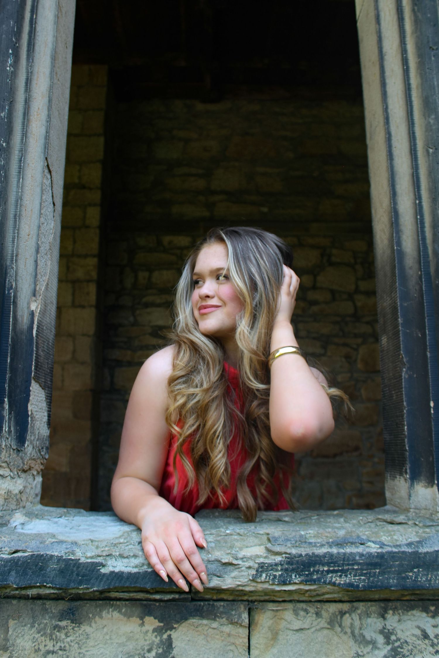 Editorial fashion photo of a woman posed leaning out of a cathedral window. Wearing her hair down and pink dress.