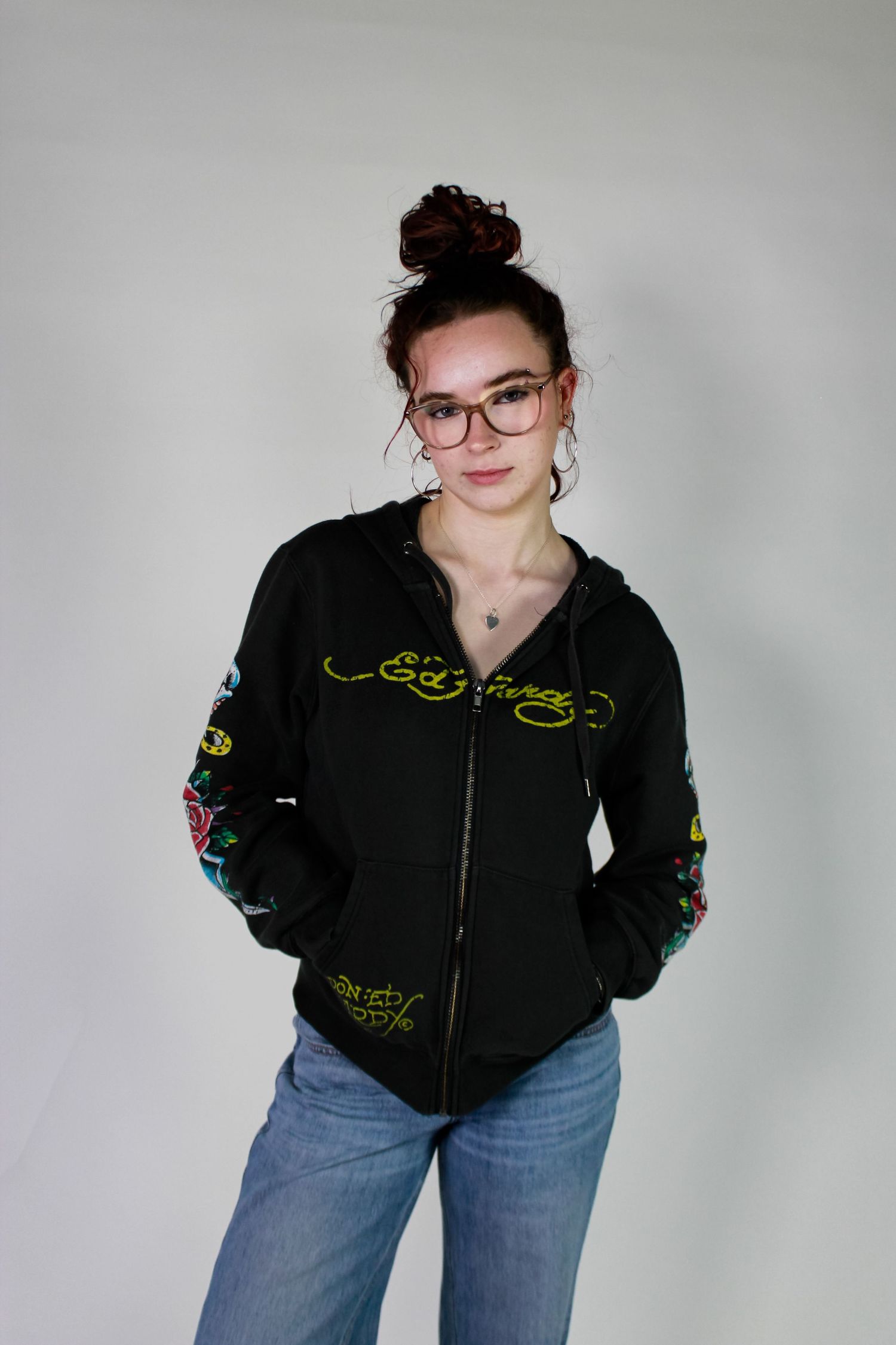 Studio portrait of a posed with her hands in her pockets. Fashion photo. Wearing her red hair in a bun, jeans and a hoodie.