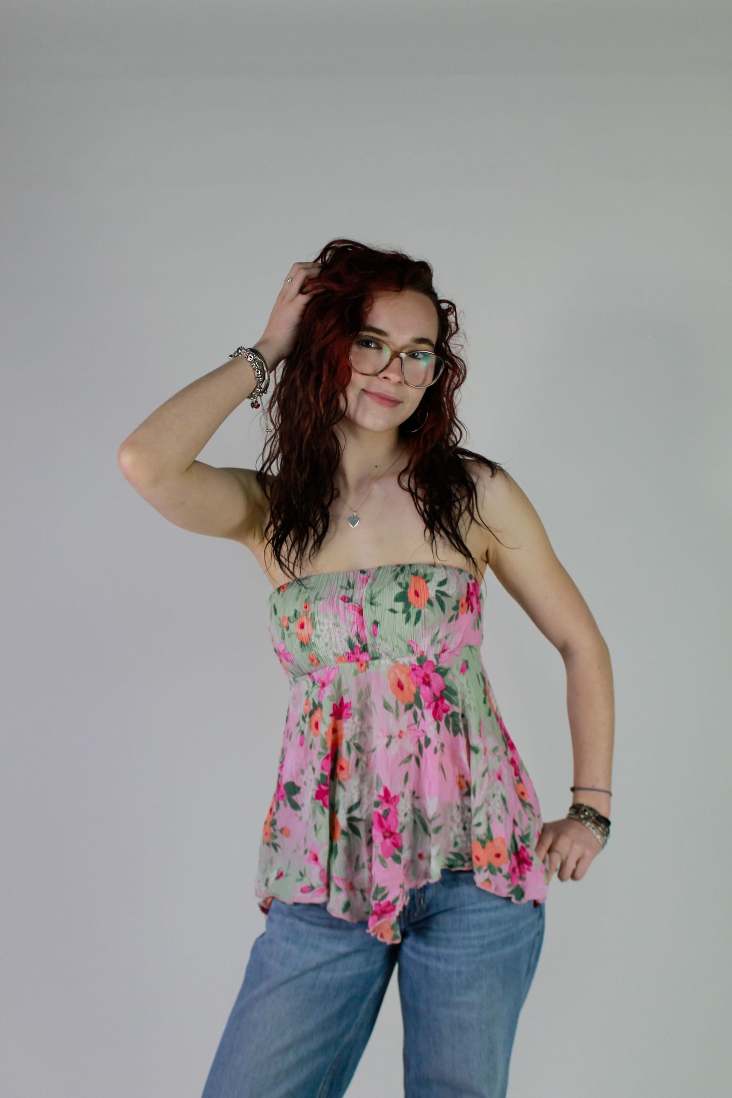Studio portrait of a woman posed. Fashion photo. Wearing her red hair down, jeans and pink floral top.