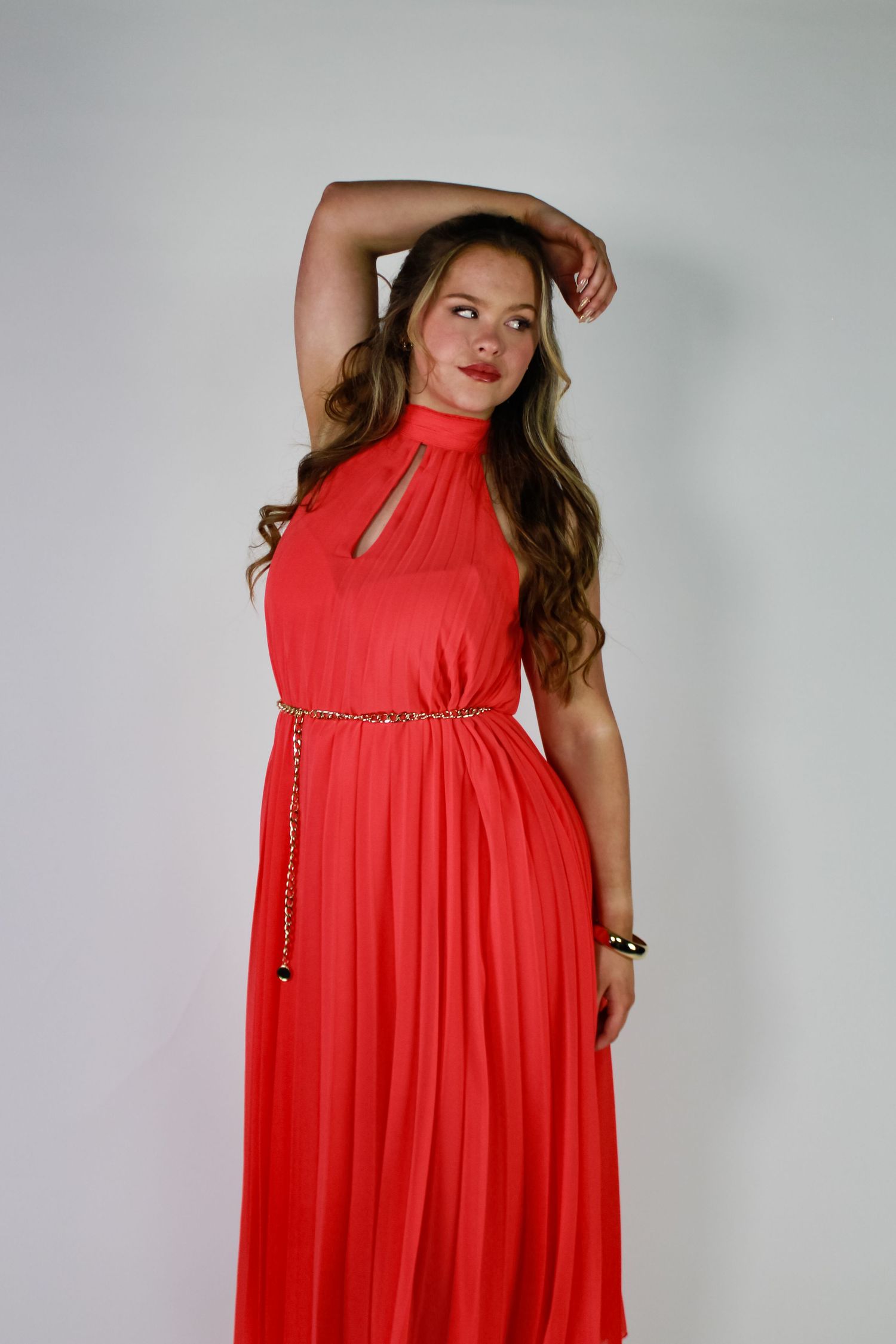 Studio portrait of a woman posing with one arm above her head. Fashion photo. Wearing a pink dress. Hair half up.
