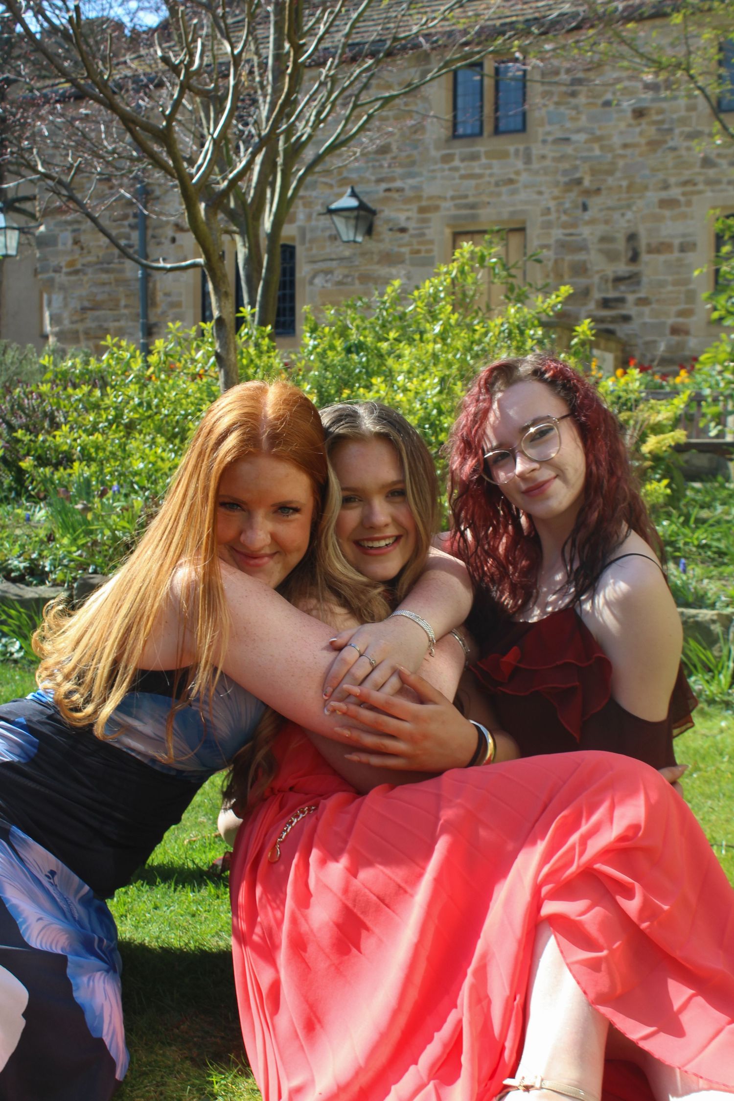 Editorial fashion portrait of three women hugging in a garden with a beautiful background.