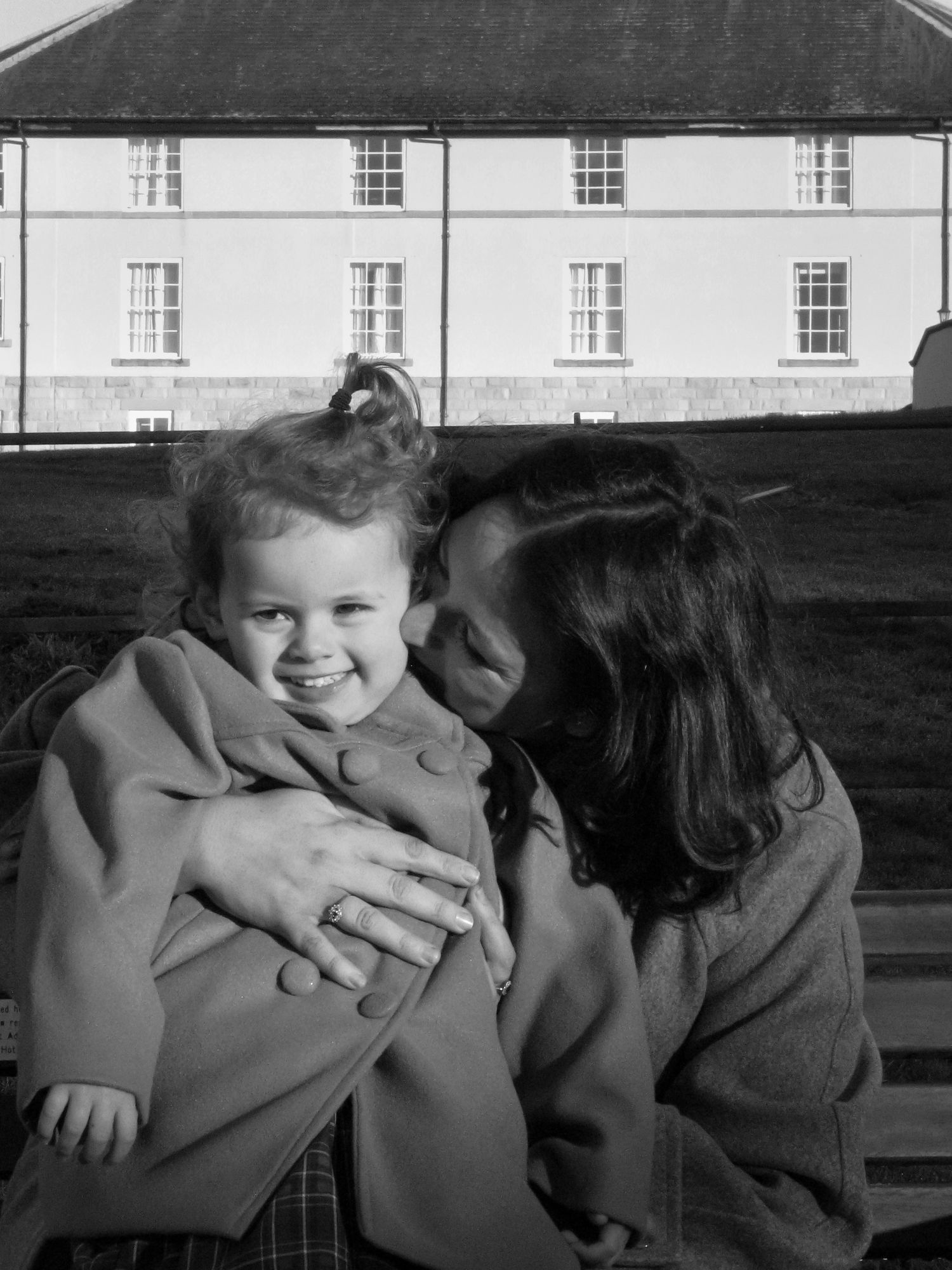 A mother hugging her daughter and kissing her on the cheek. Family photoshoot. Black and white.