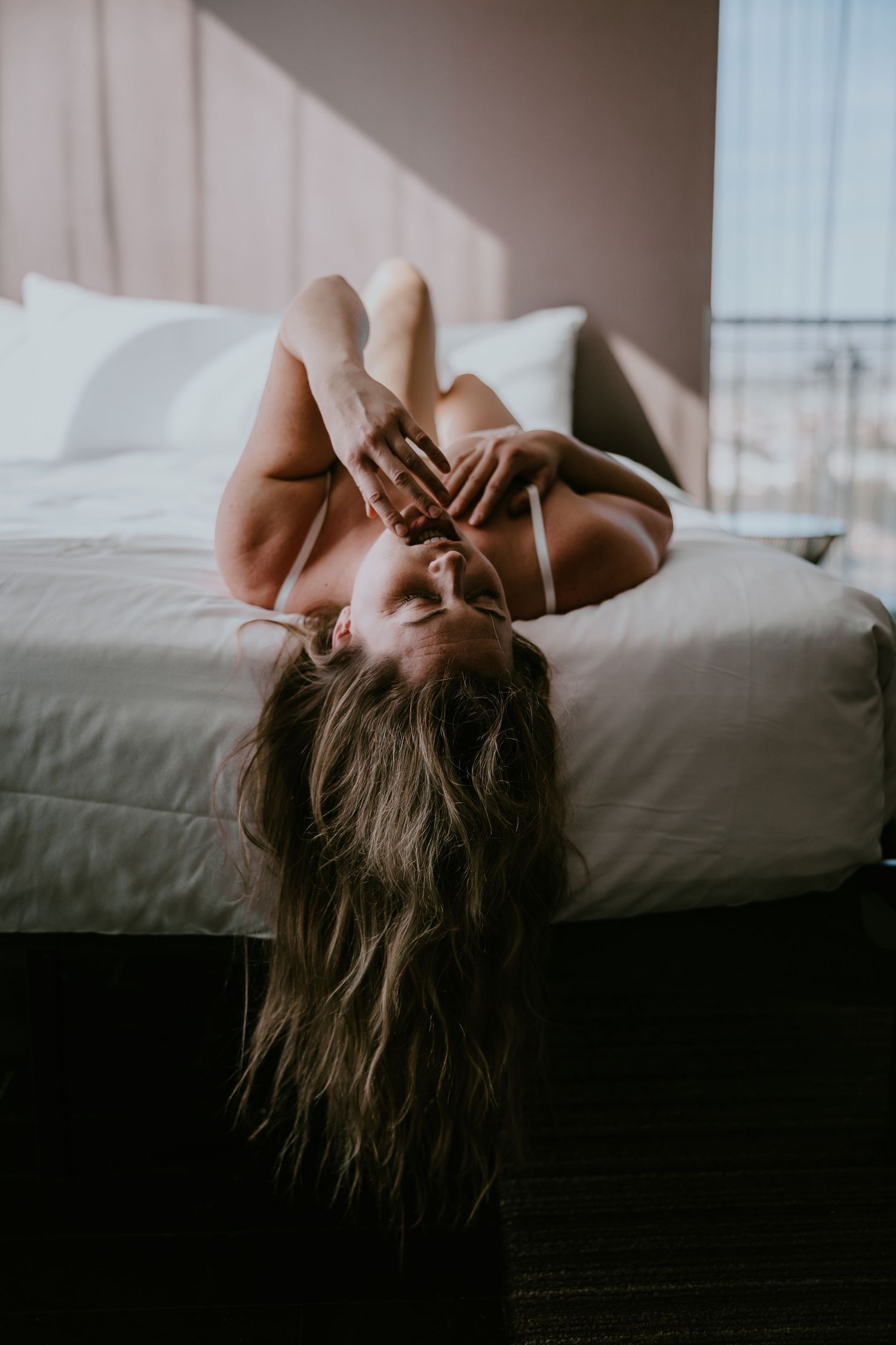 Intimate bedroom portrait with soft morning light filtering through curtains.