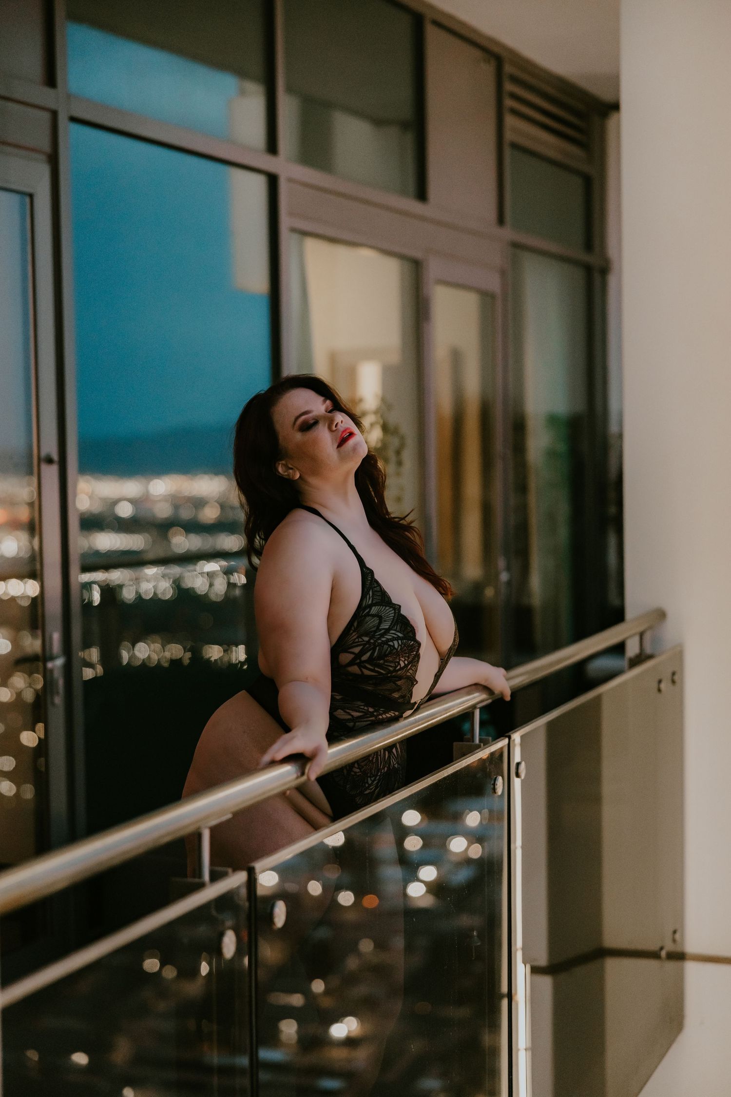 Moody nighttime balcony photoshoot with city lights in background.