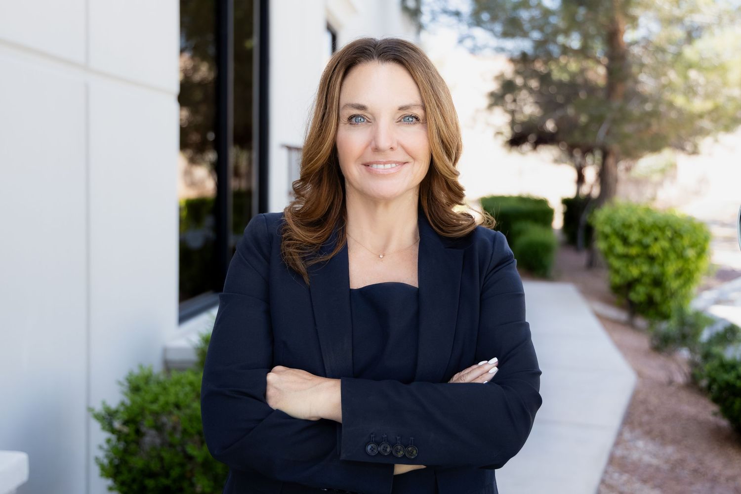 Professional businesswoman in black blazer smiling with arms crossed outside modern office building.
