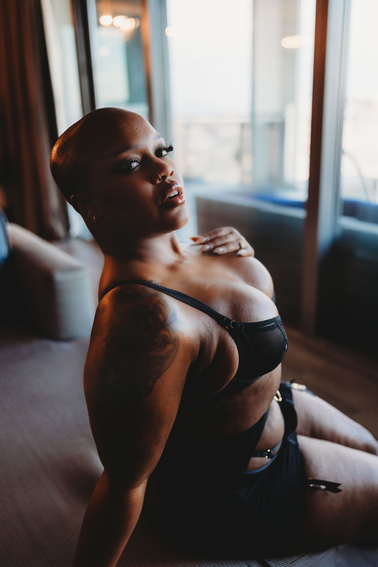 Person in black lingerie poses on floor with natural window lighting.