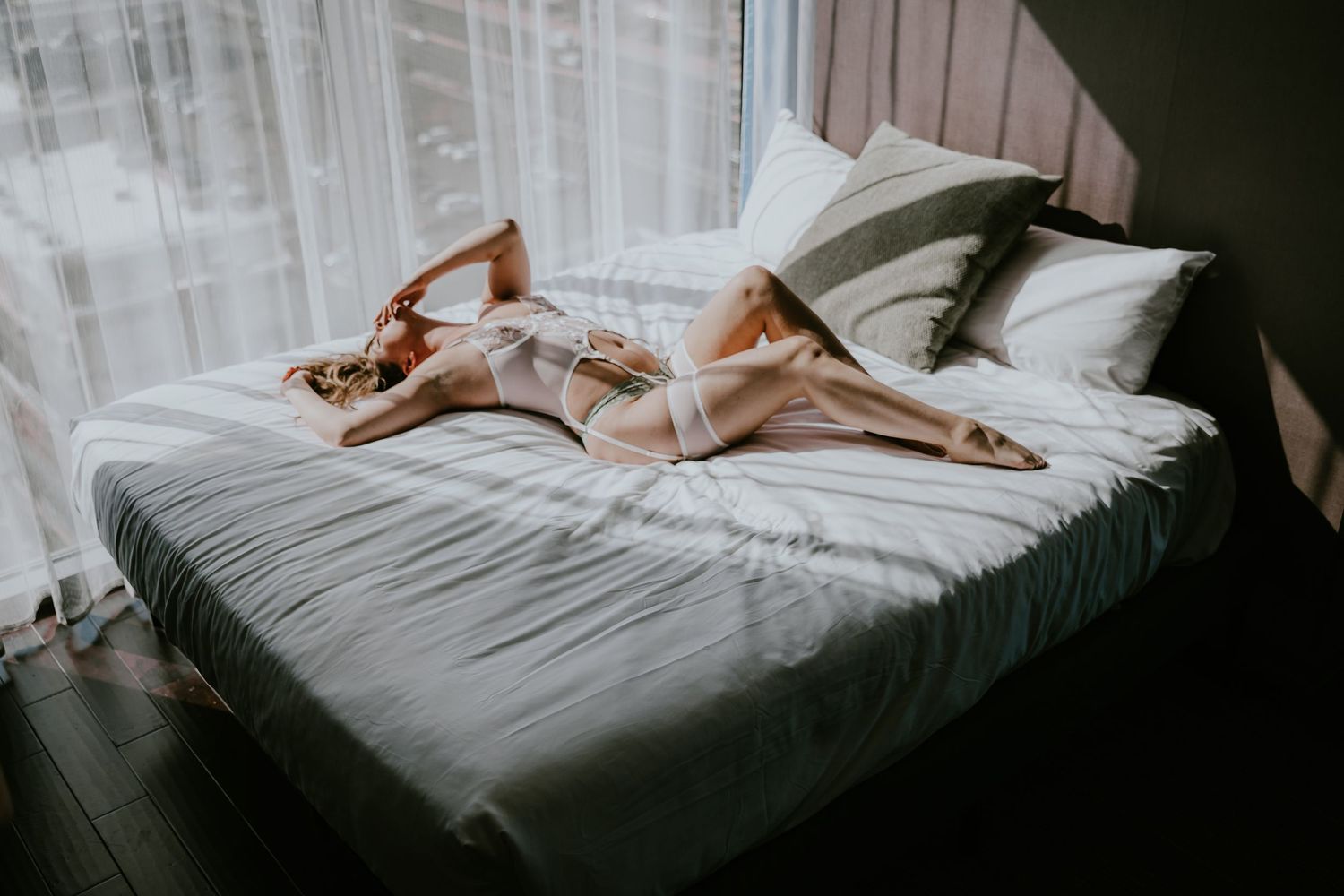 Dreamy boudoir scene with white bedding and morning light through window.