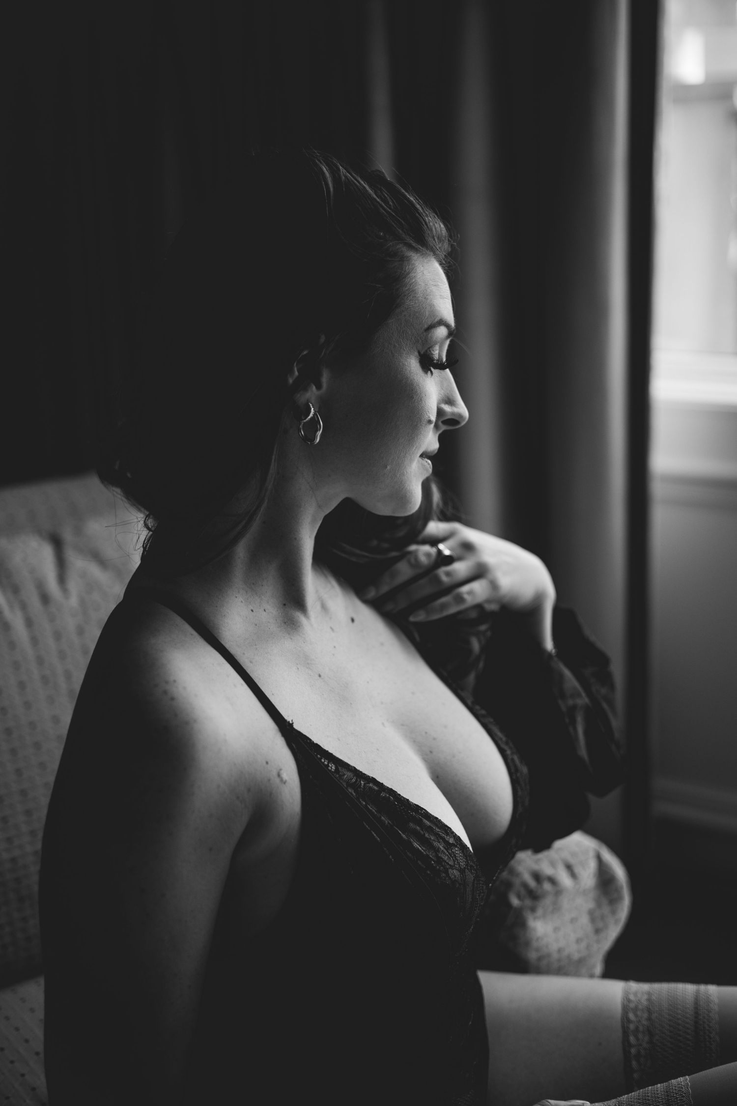 Side profile portrait in black and white showing subject in lace lingerie near window.