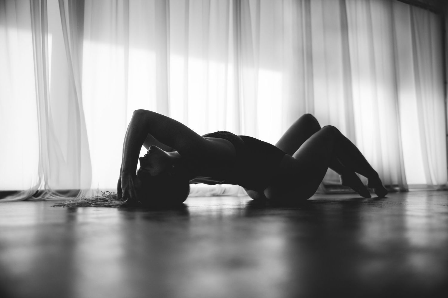 A dramatic black and white silhouette shows a figure lying on the floor against a bright window backdrop.