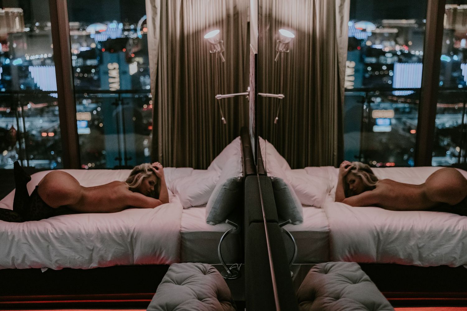 Artistic boudoir photo of a figure reclining on white bedding in moody lighting.