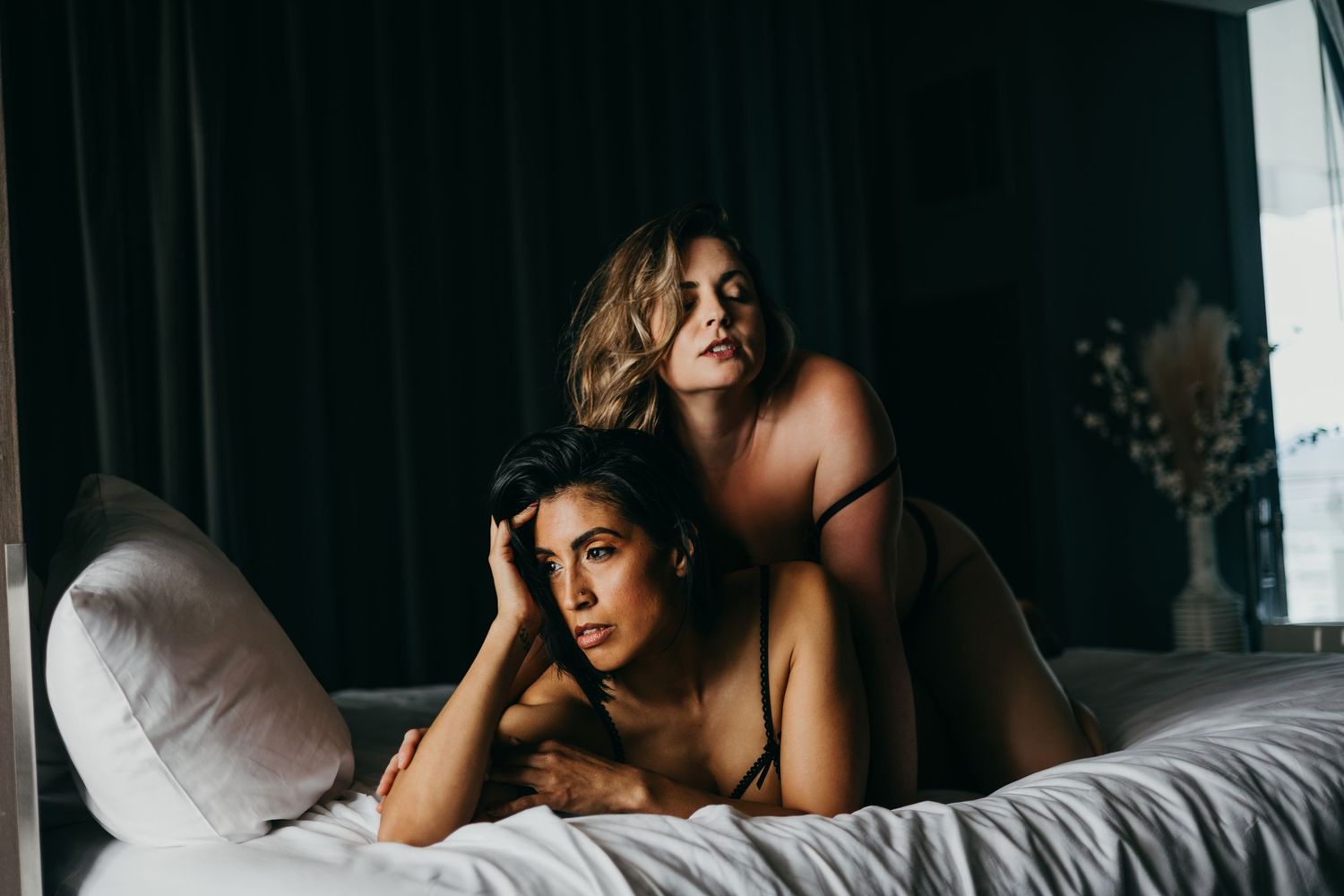 A group of people lounge together on a bed in a moody, intimate setting with soft lighting.