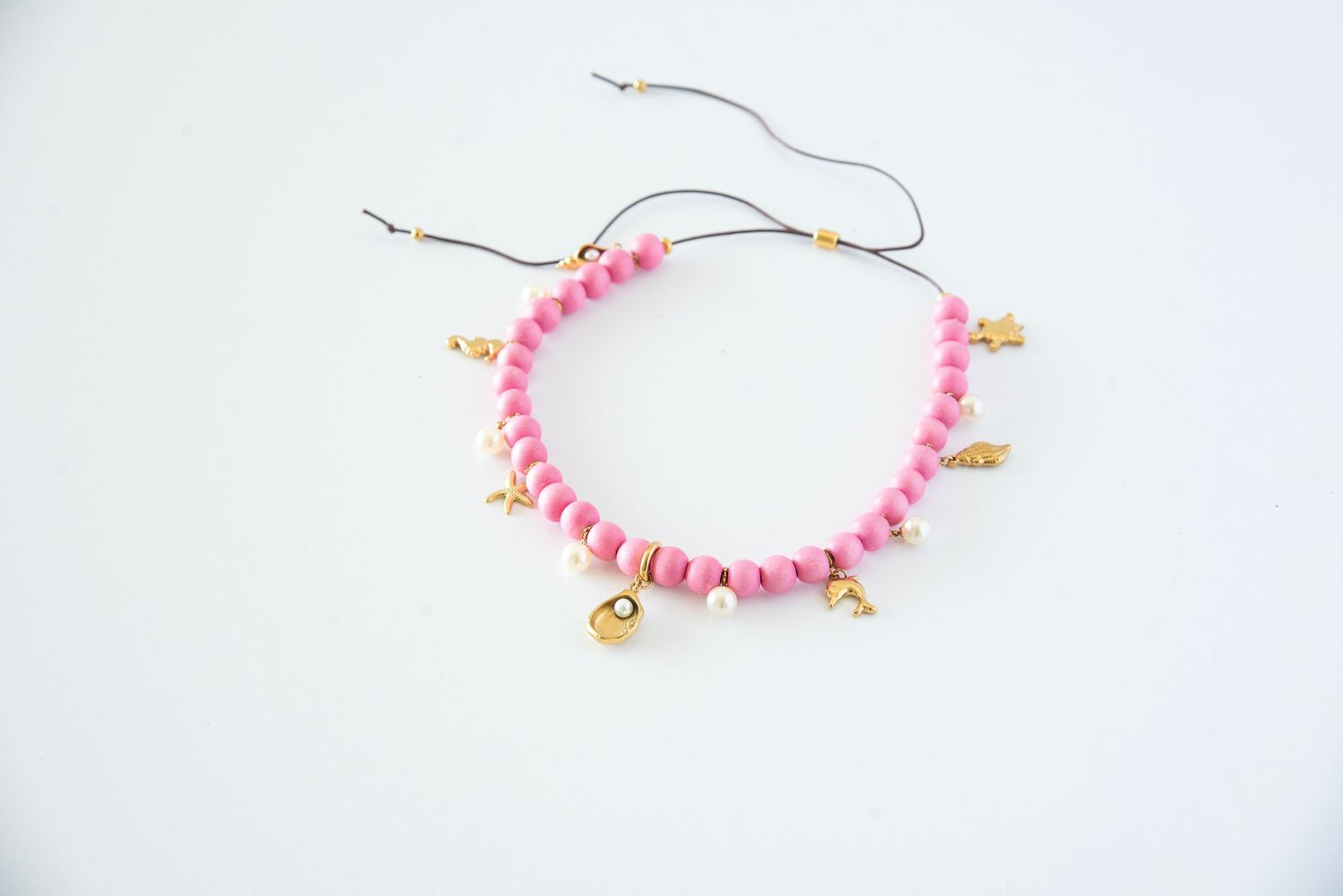 Pink wooden bead bracelet with small gold charms displayed on white surface.