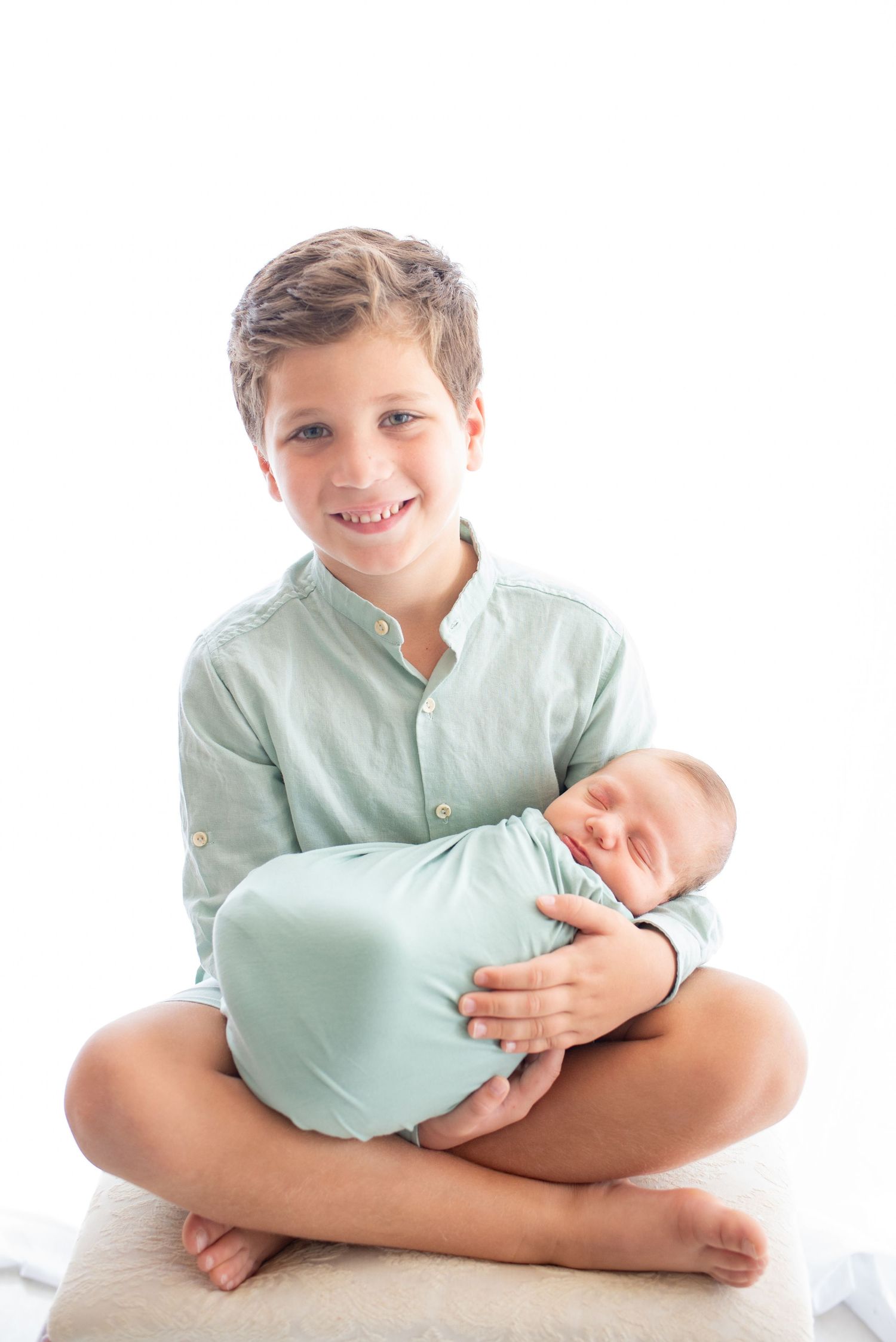 Siblings sharing a tender moment in matching mint green outfits against white background.