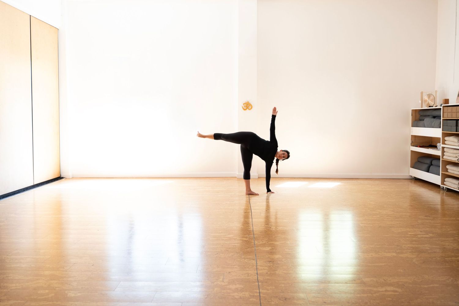 A dancer performs an arabesque pose in a sunlit dance studio with wooden floors and white walls.