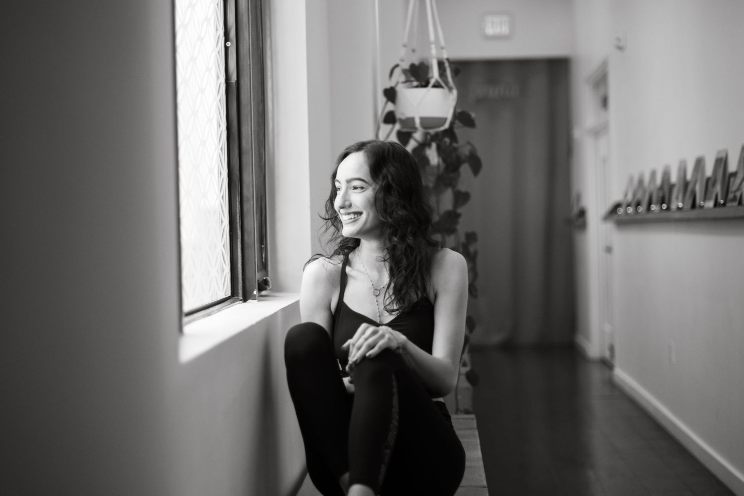 Black and white photo of someone sitting by window in casual attire, smiling while looking away.