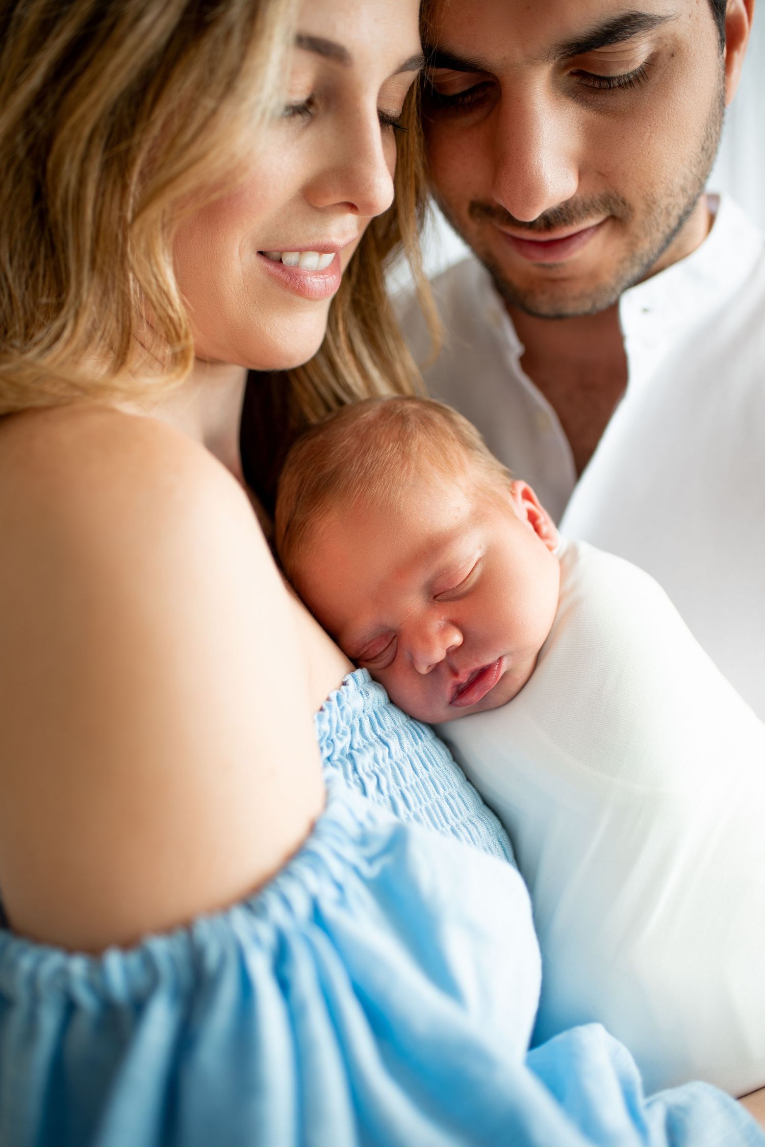 Couple wearing white and blue outfits embracing in soft light.