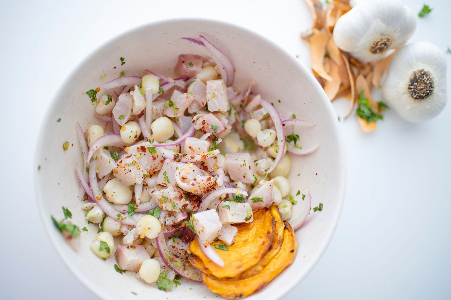 A bowl of seafood ceviche with citrus and fresh herbs arranged in a circular pattern on a white plate.