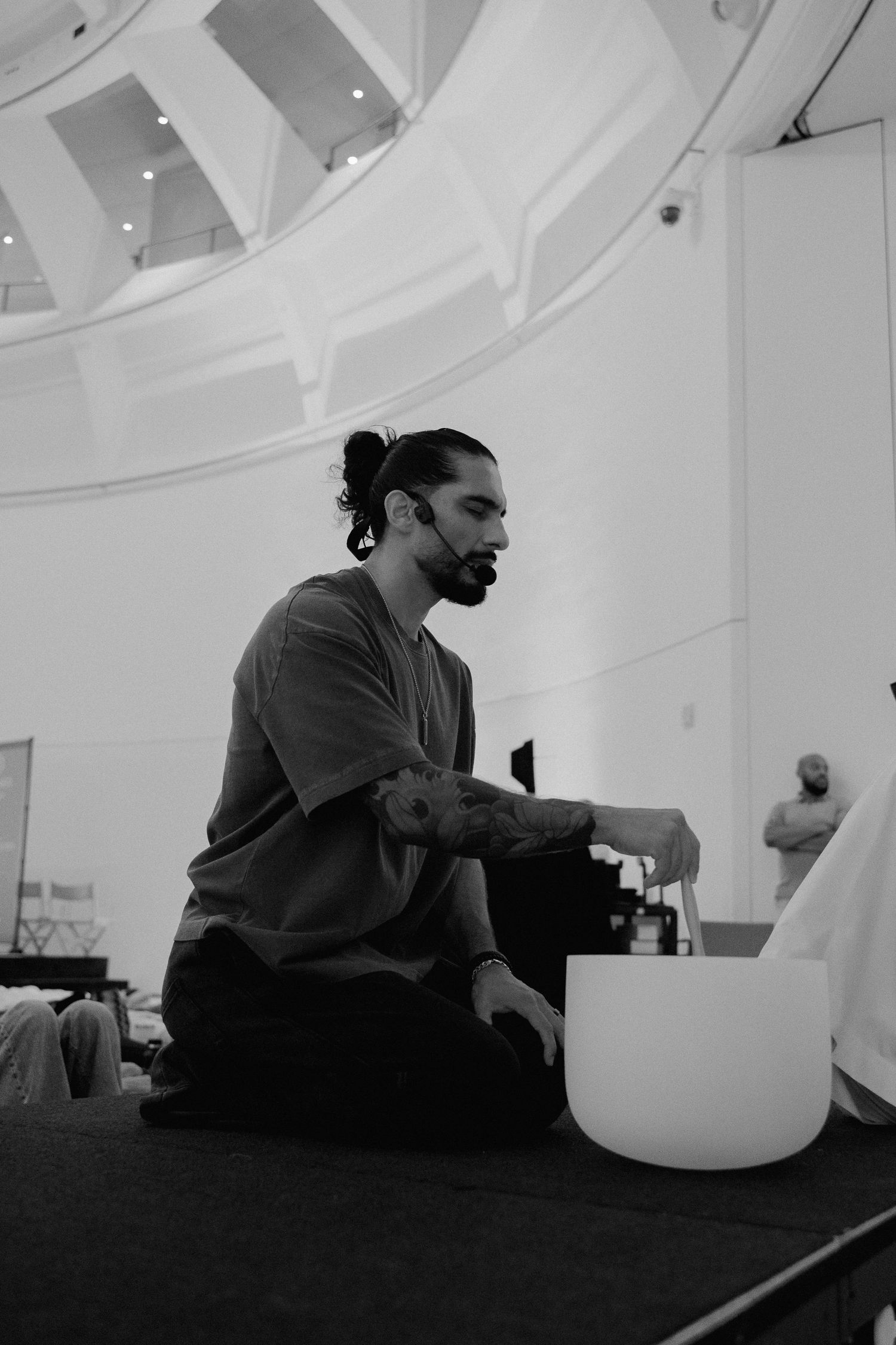 Man playing crystal singing bowl seated cross-legged in a bright domed room during sound bath.