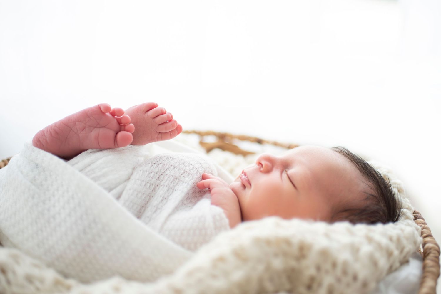 Sleeping newborn baby resting peacefully in woven basket with white bedding.
