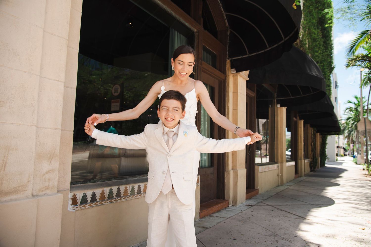 Wedding party members share candid moments along a palm-lined colonnade.