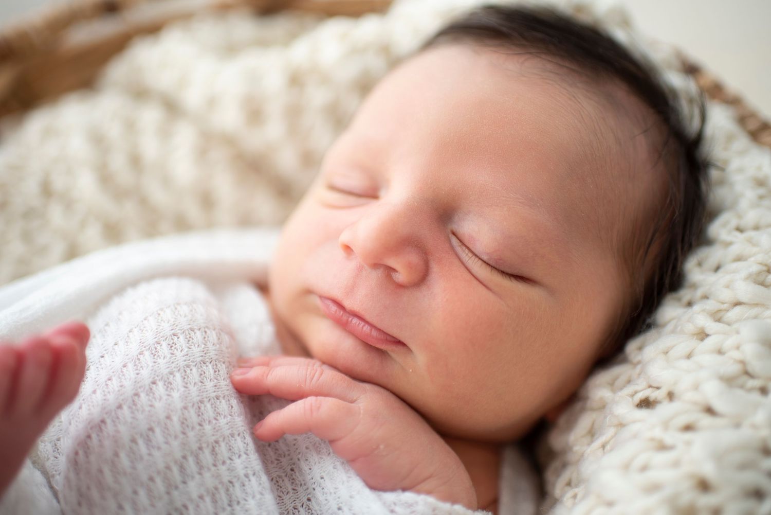 Sleeping newborn baby wrapped in soft white blanket during professional photo session.