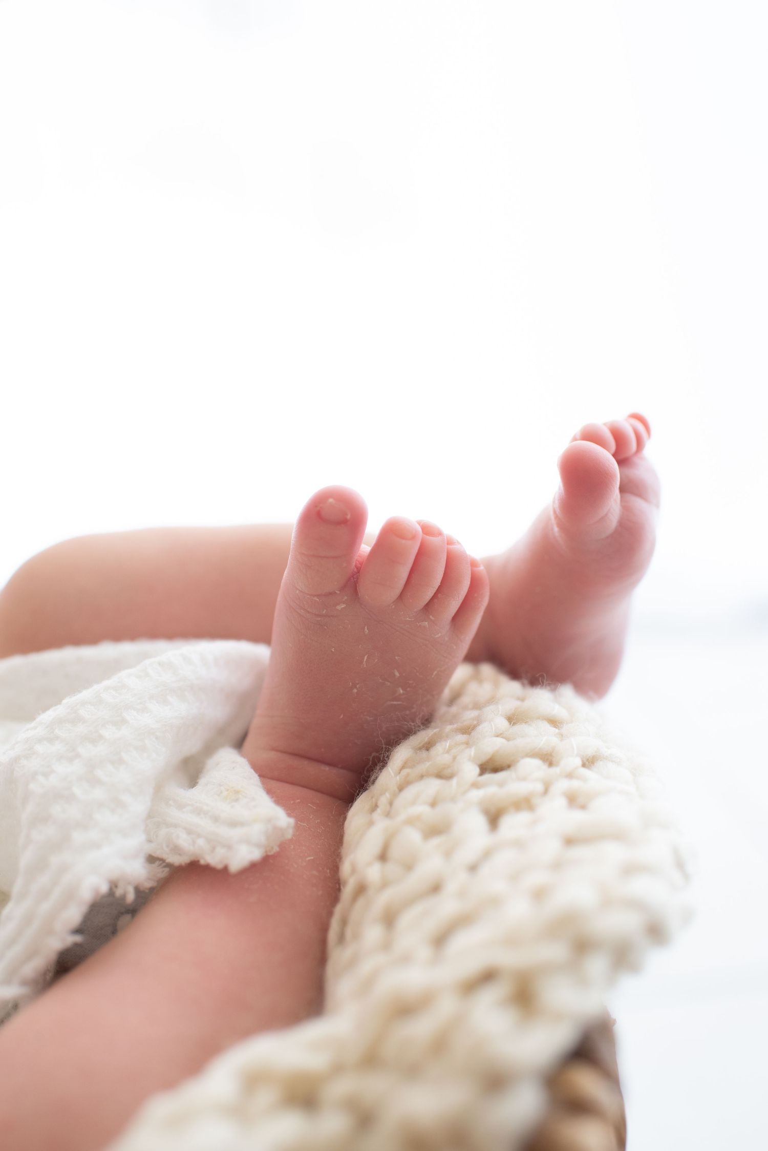 Close-up of tiny newborn feet resting on soft cream knitted blanket.