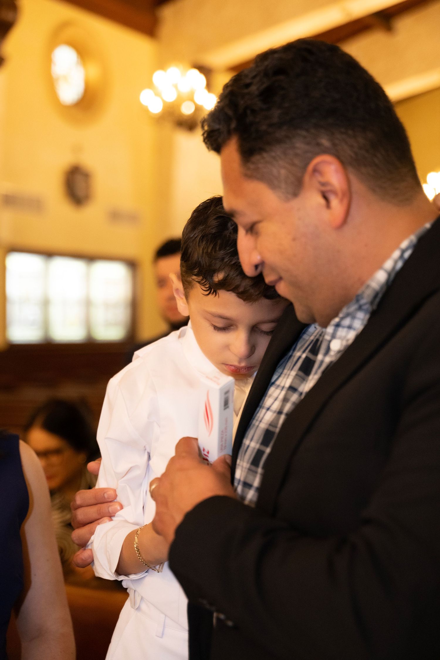 A man and young boy pray together in a church, the boy dressed in white for a religious ceremony.