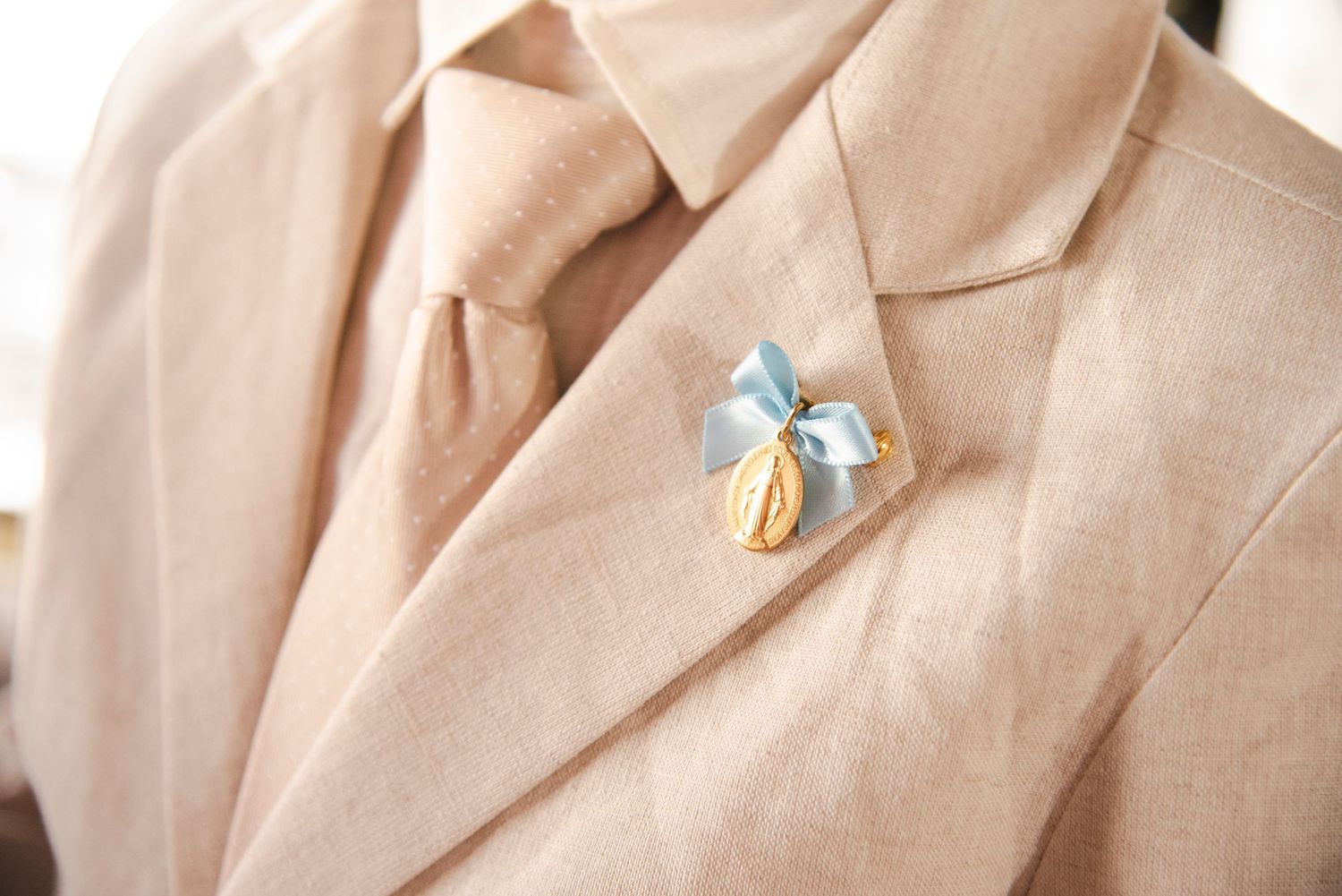Close-up detail of a beige linen suit jacket with delicate butterfly pin accessories.