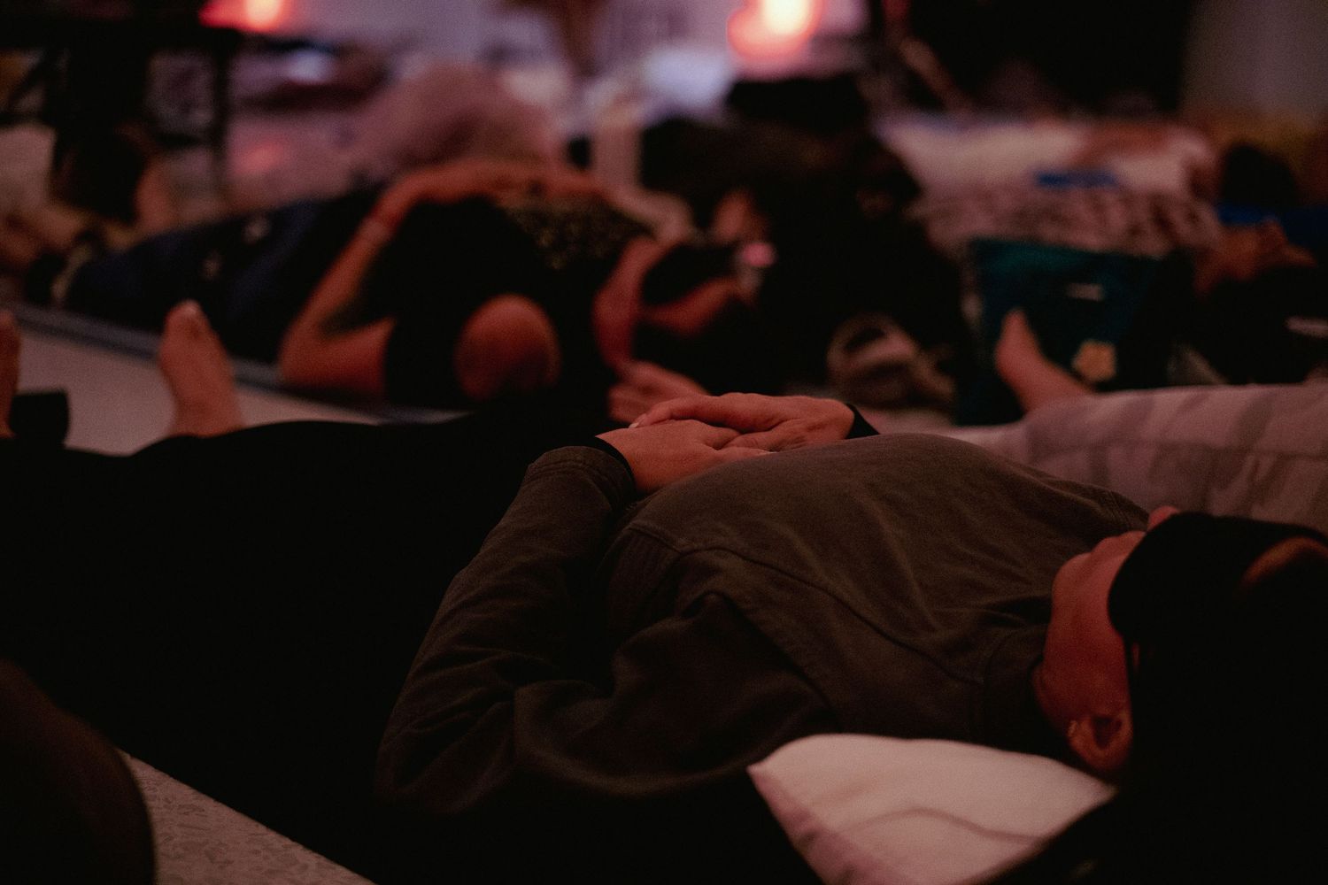 People lying down in a dimly lit room during a guided relaxation or yoga nidra meditation session.