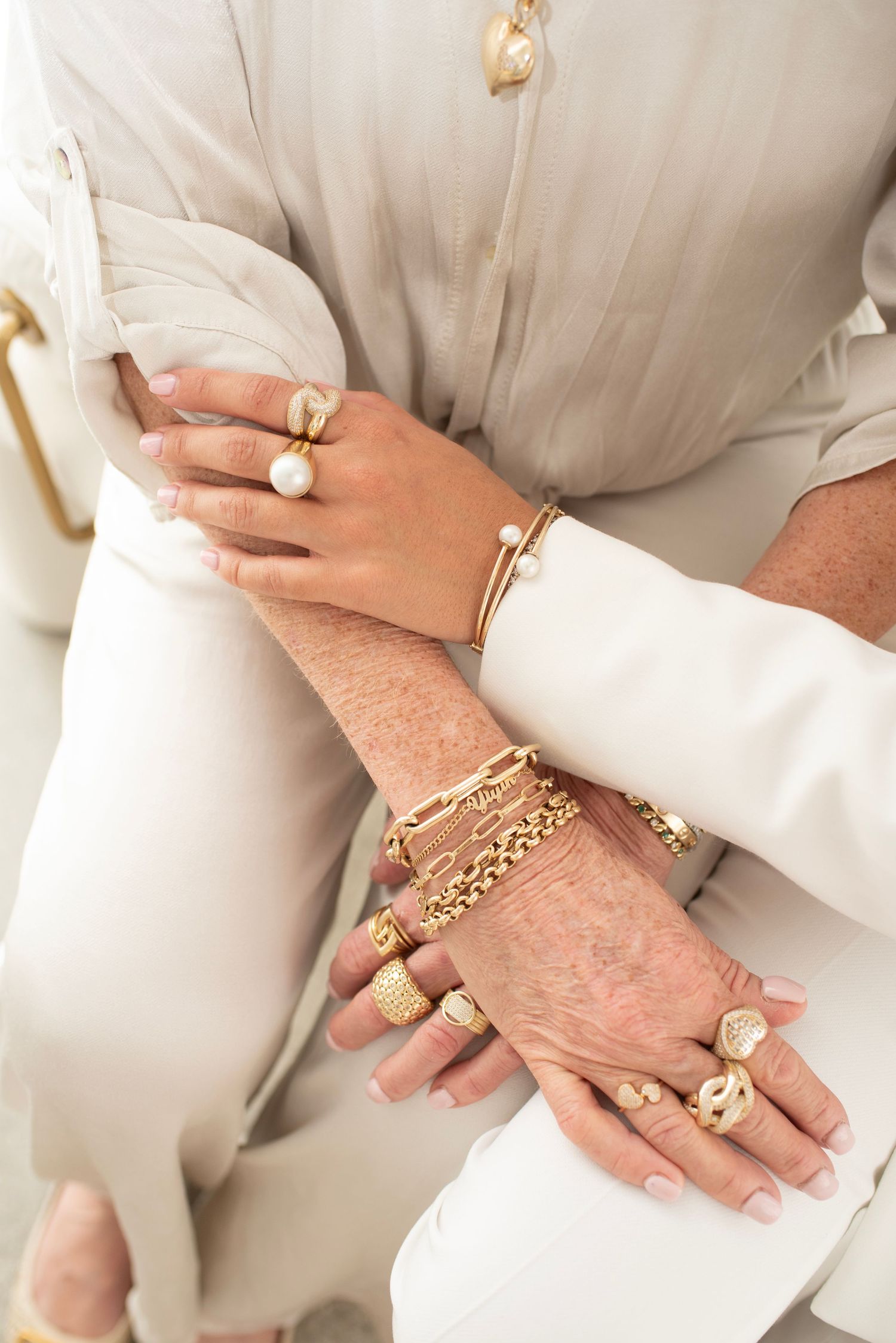 Close-up shots of hands wearing multiple gold rings and chain bracelets with a white sleeve backdrop.