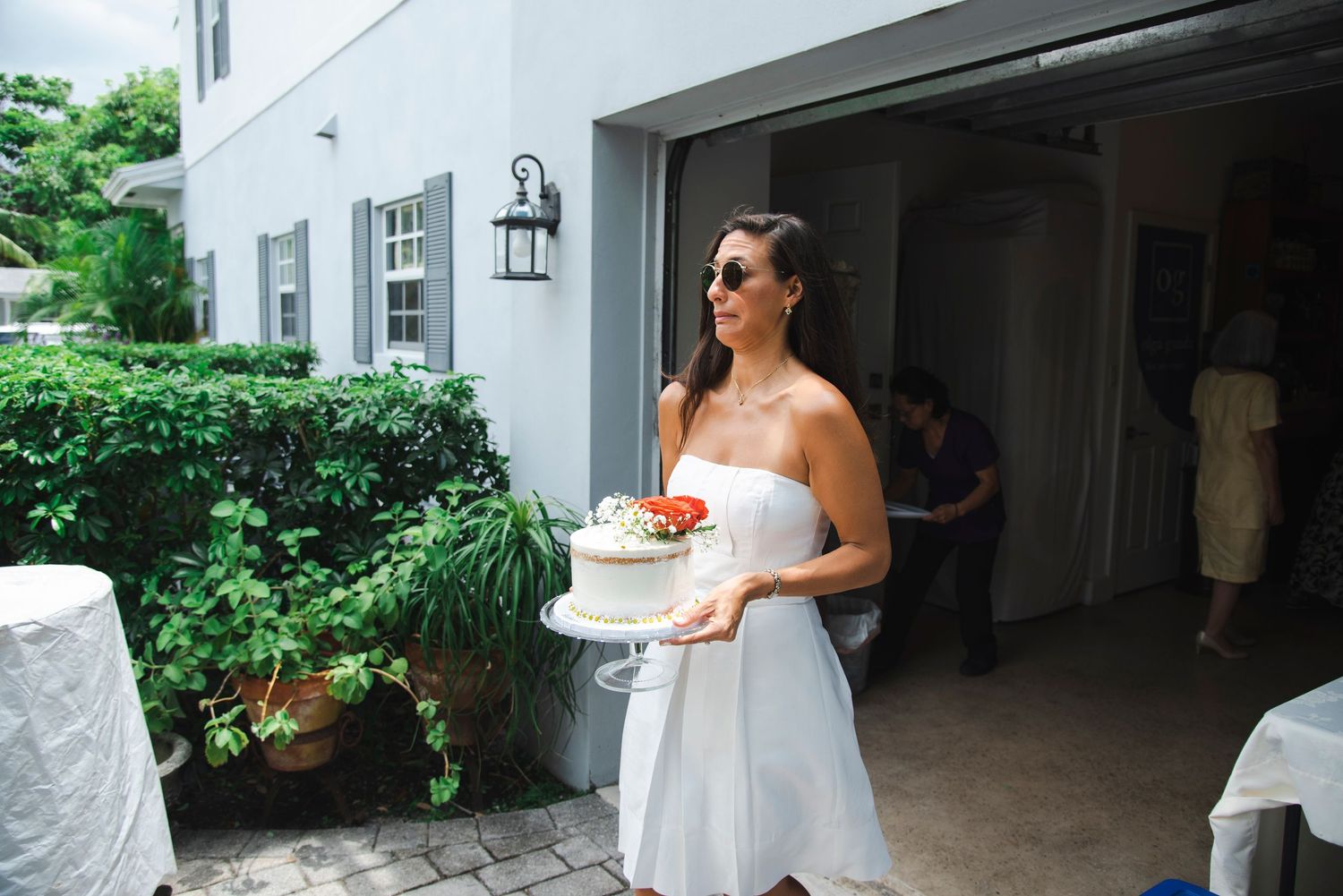 An outdoor celebration at a white house with people gathered on the patio.