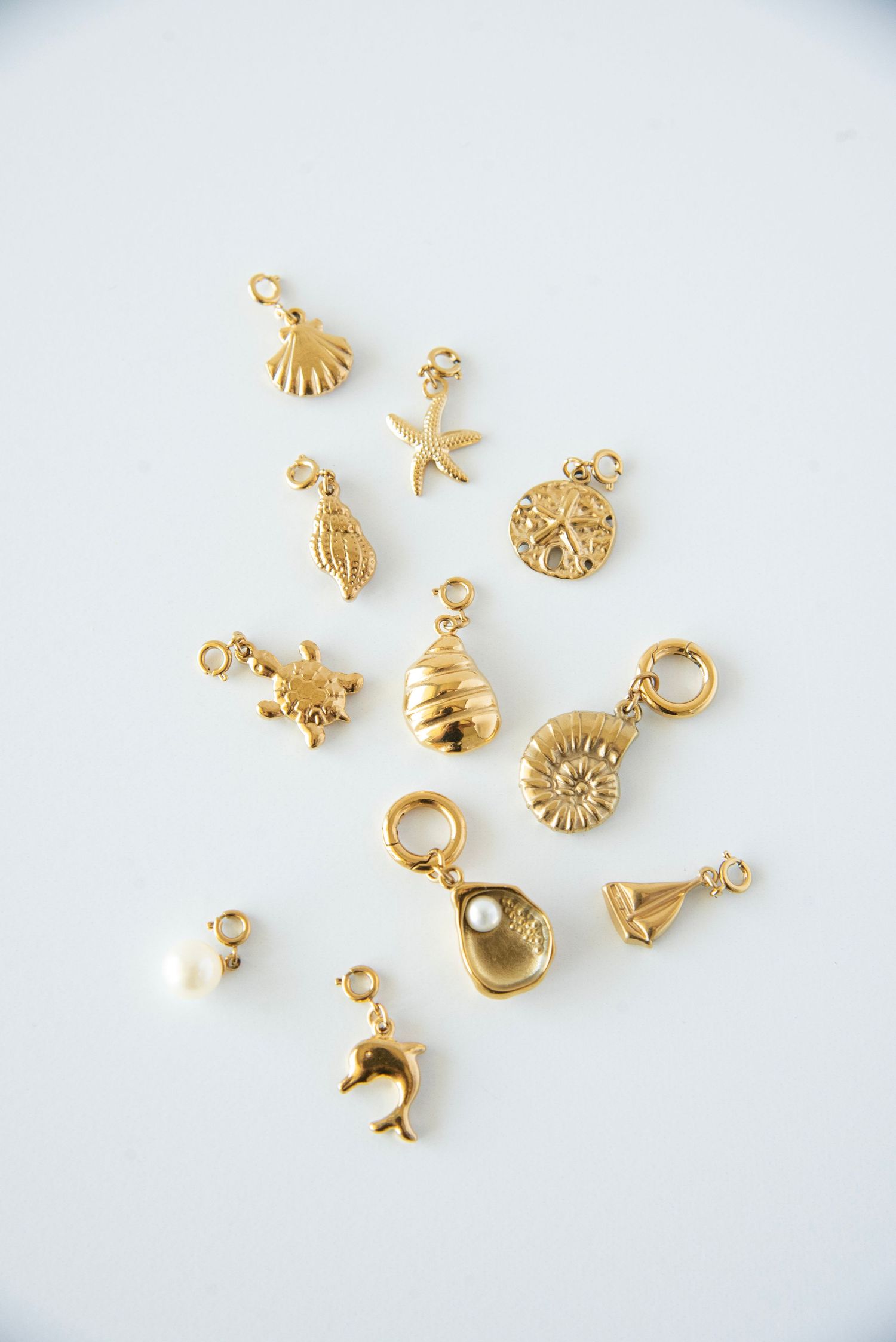 Collection of small gold seashell and ocean-themed jewelry charms displayed on white surface.