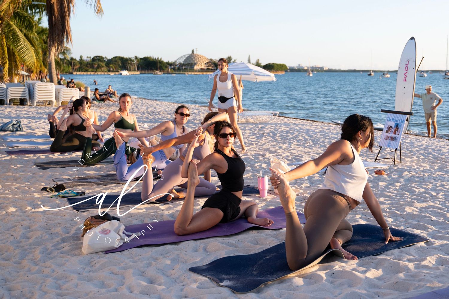 People exercising together on a sandy beach during sunset with ocean waves in the background.