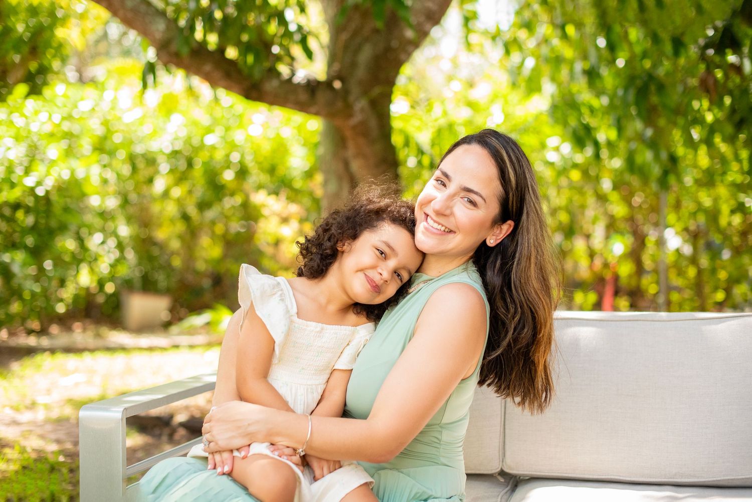 A tender embrace shared between two people sitting outdoors in a sun-dappled garden setting.